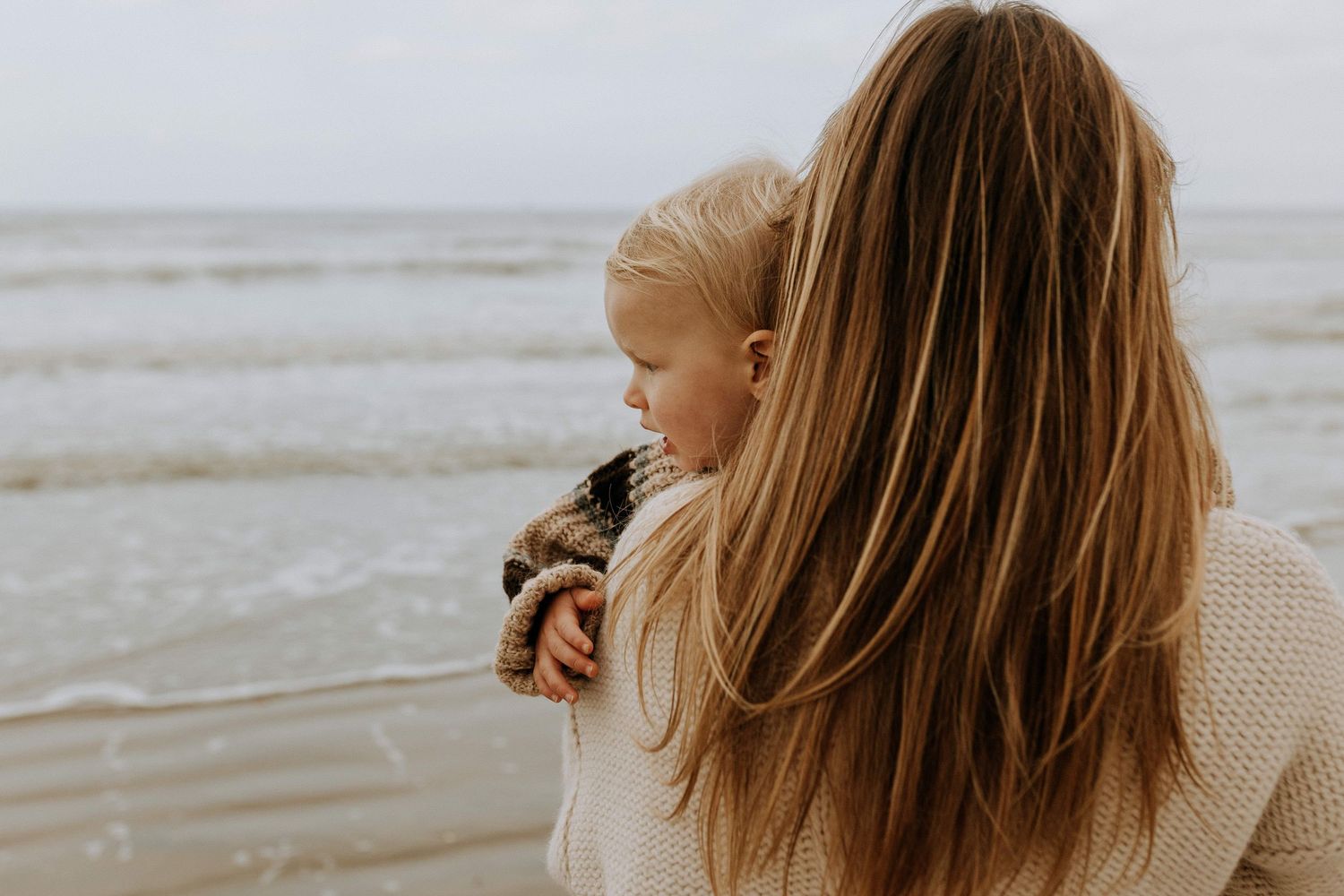 Maman tenant son enfant face à la mer, séance photo famille naturelle et intime réalisée par une photographe à Lille et en France