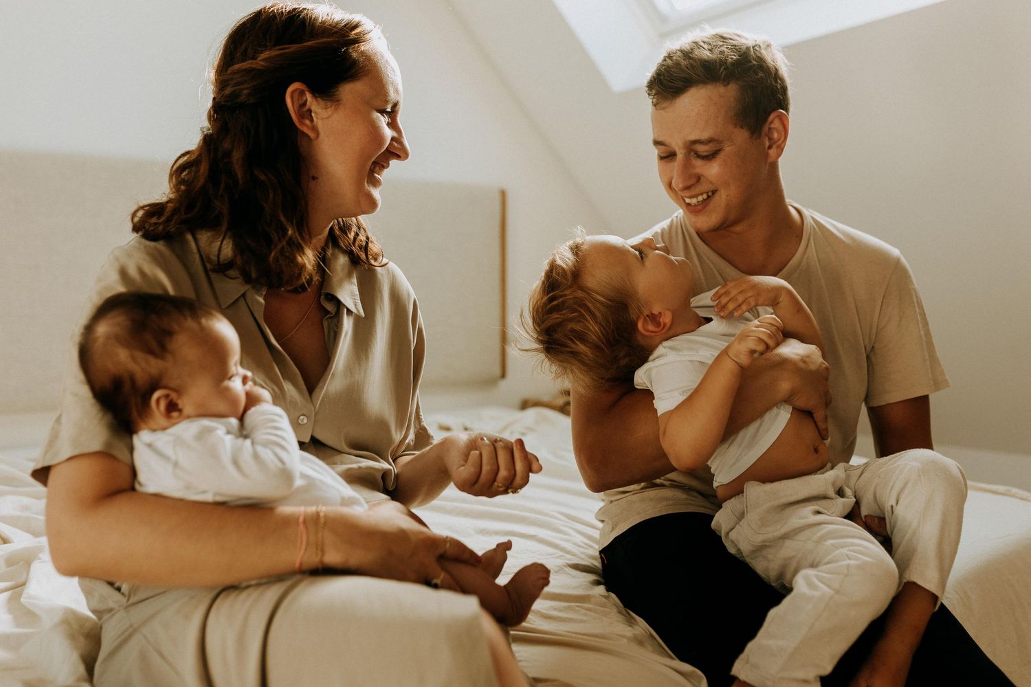 Séance photo famille à domicile à Lille, parents assis sur un lit avec leur bébé dans une ambiance douce et naturelle