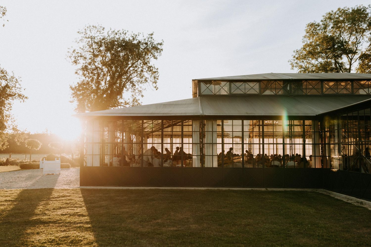 Salle de réception de mariage baignée de lumière dorée en fin de journée, invités attablés à l’intérieur.