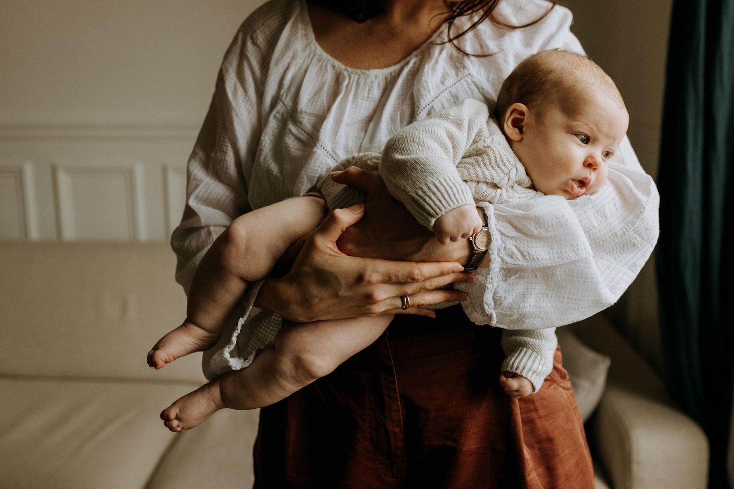 Séance photo naissance à domicile : un bébé dans les bras de sa maman, lumière naturelle et instant tendre capturé sans mise en scène.