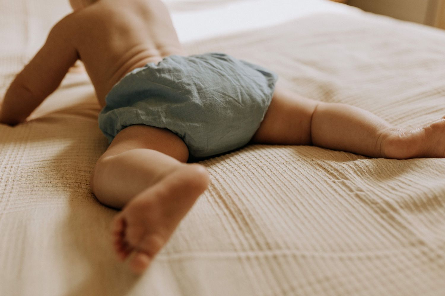 Séance photo bébé à domicile à Lille, détail des jambes d’un nourrisson allongé sur un lit, ambiance chaleureuse et naturelle