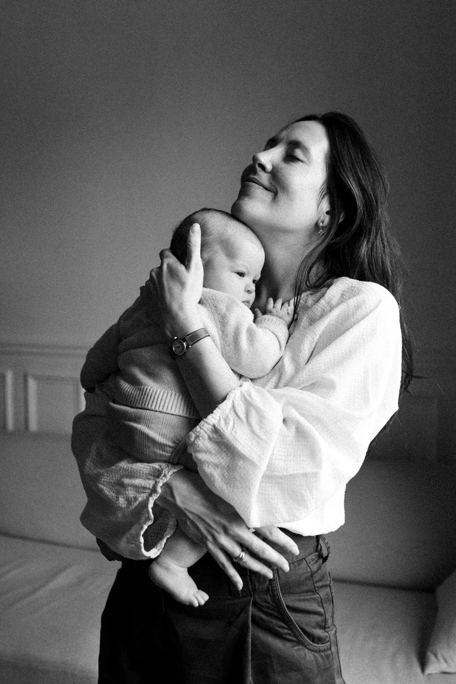 Photographie de naissance en noir et blanc, maman tenant son bébé lors d’une séance photo naturelle à domicile.