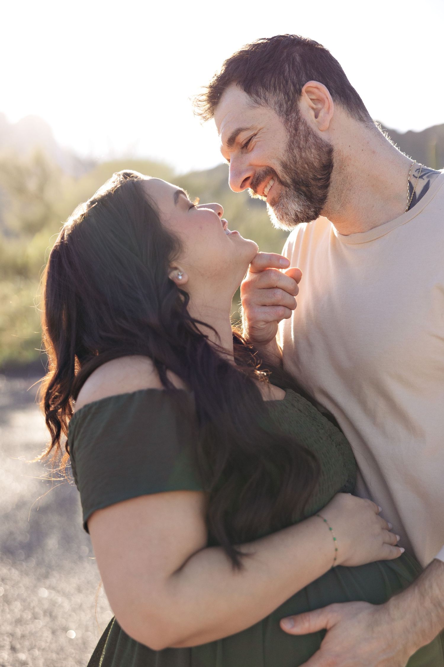 A couple shares a romantic moment outdoors, smiling and holding hands in warm golden sunlight.