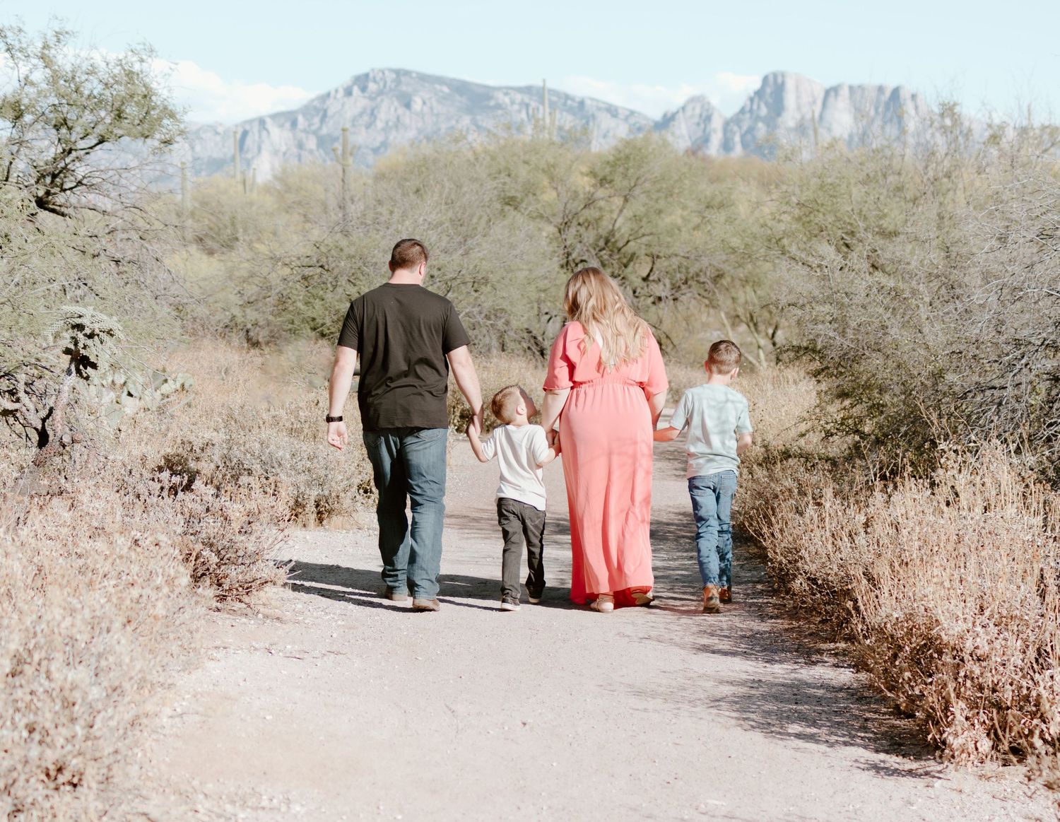 A group of hikers walk along a desert trail with rugged mountain peaks visible in the background.