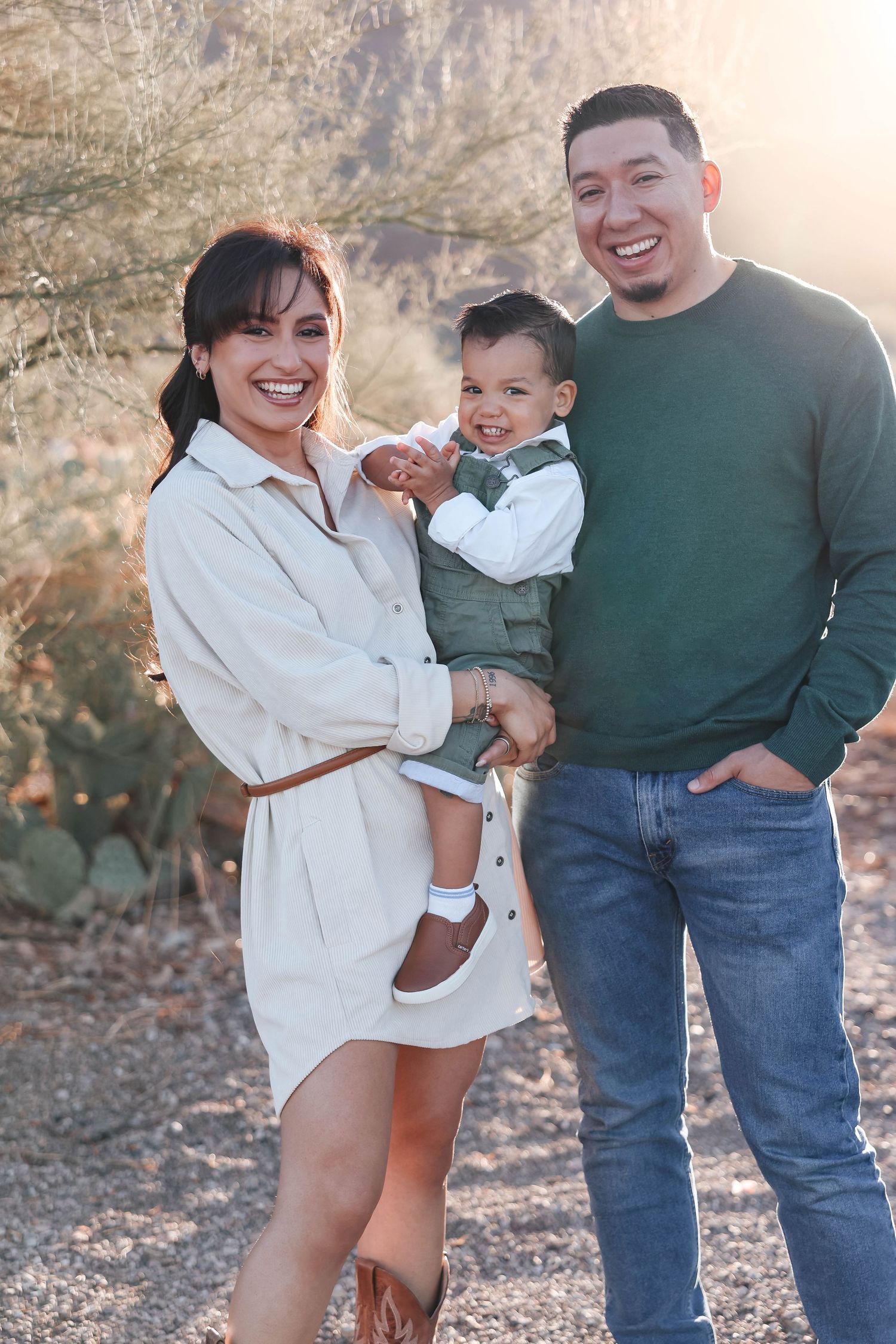 A couple poses playfully in a desert landscape with cacti and golden sunlight during a photo session.