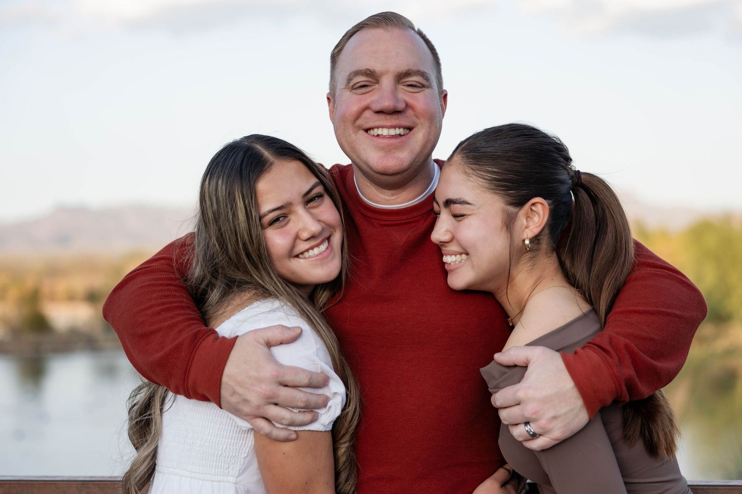 A family wearing red sweaters poses together outdoors for holiday photos at sunset.