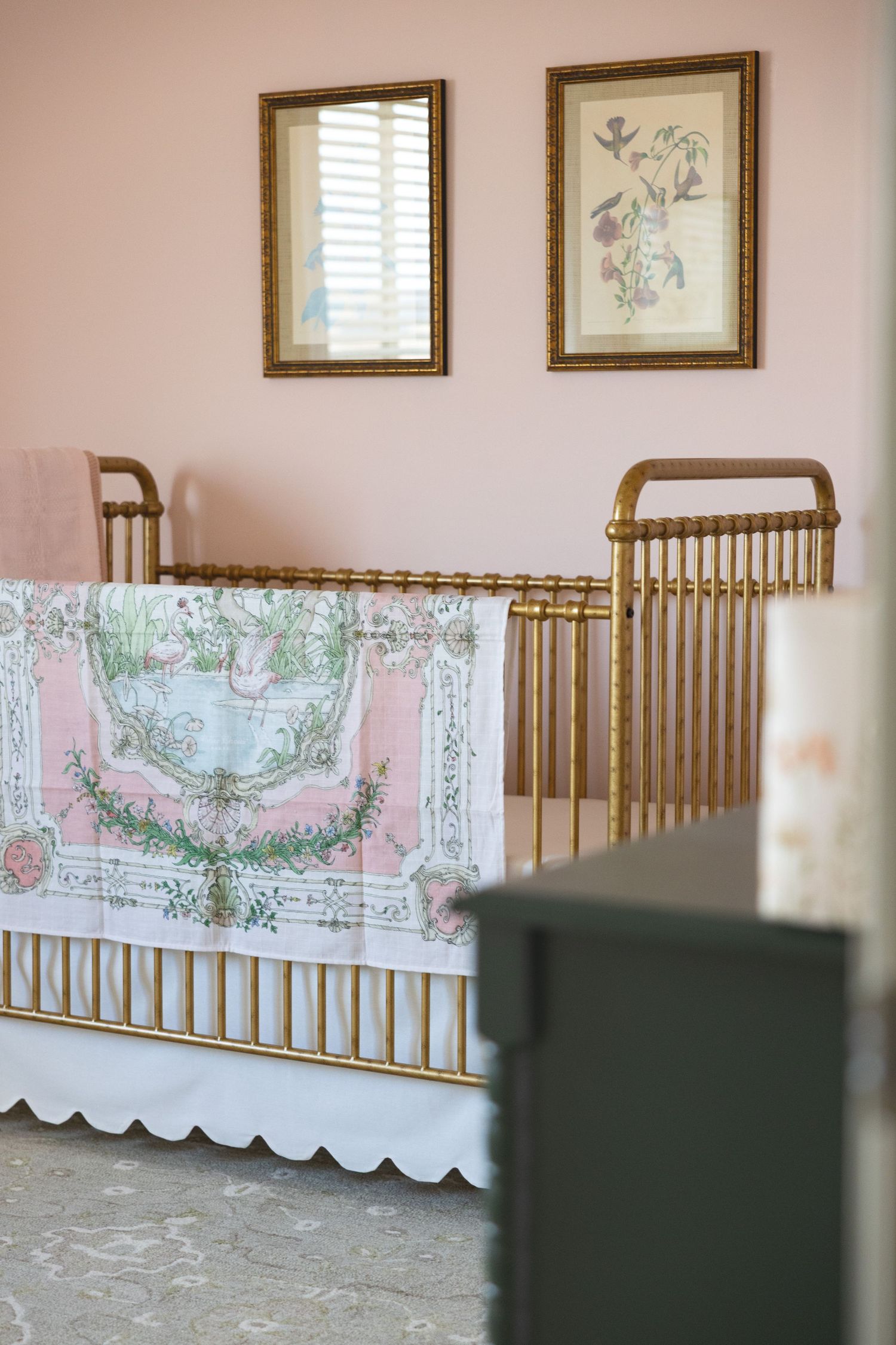 Gold spindle crib with pink floral bedding in a blush nursery with framed botanical art above.