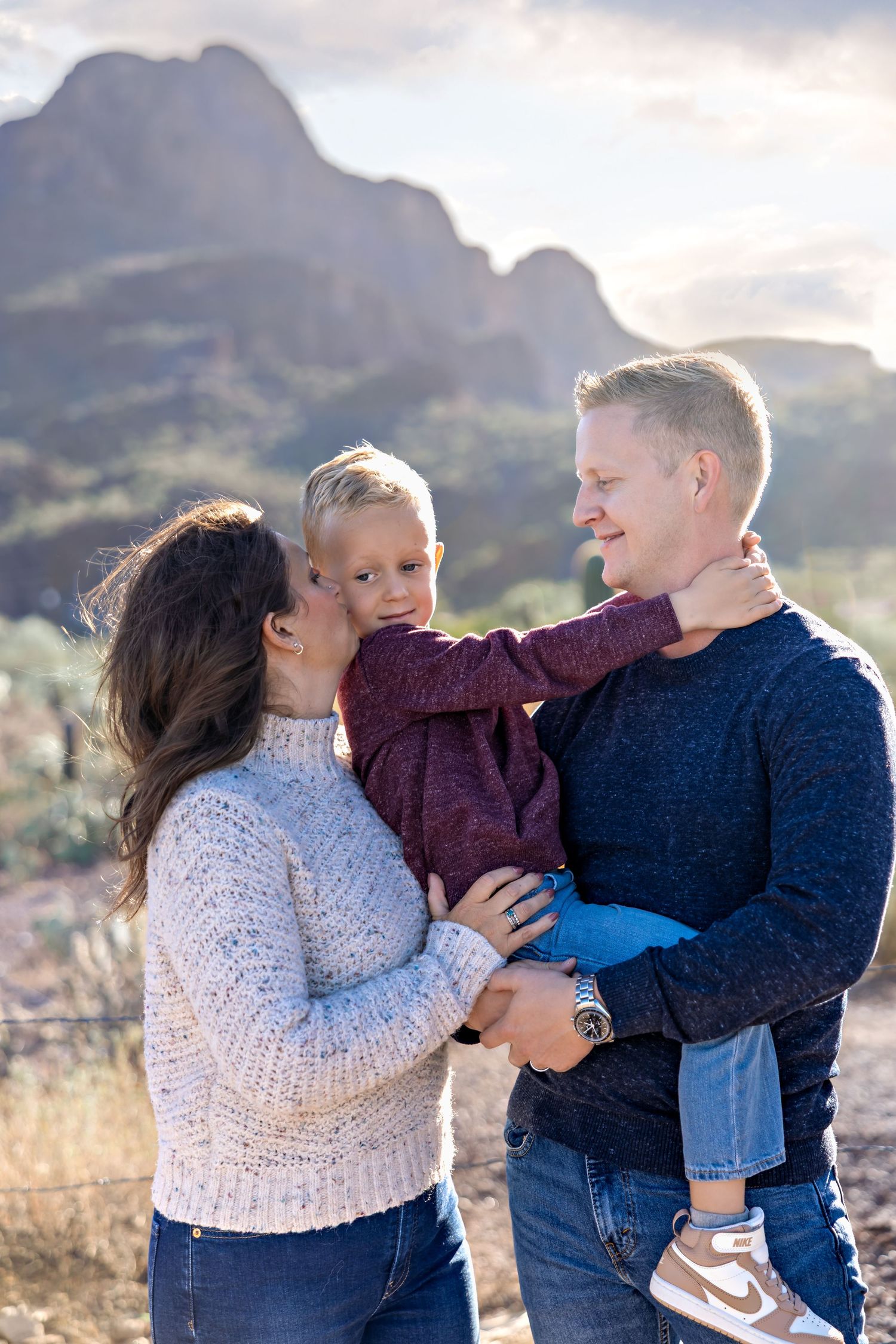 Family shares a tender moment together against a backdrop of rugged desert mountains during golden hour.
