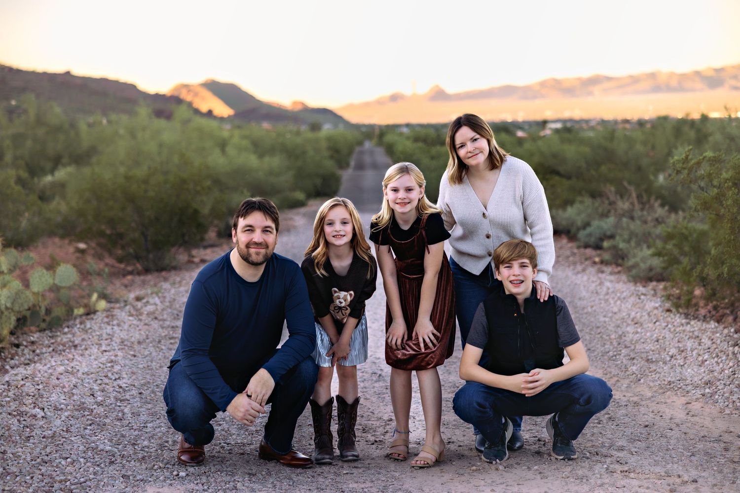 A group poses together on a desert hiking trail with mountains and desert landscape in the background at sunset.