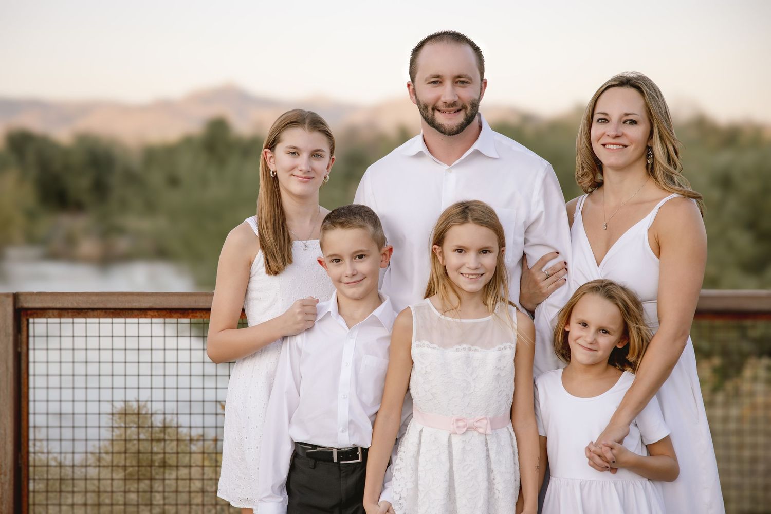 A family wearing coordinated white outfits poses together outdoors during a golden hour photoshoot in nature.