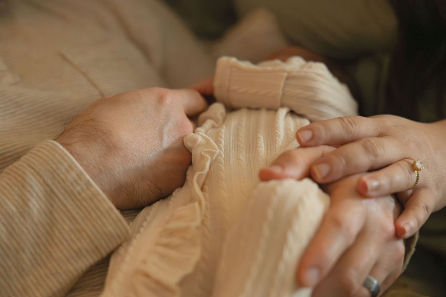 Close-up of two adults tenderly holding a newborn baby wrapped in soft beige fabric.