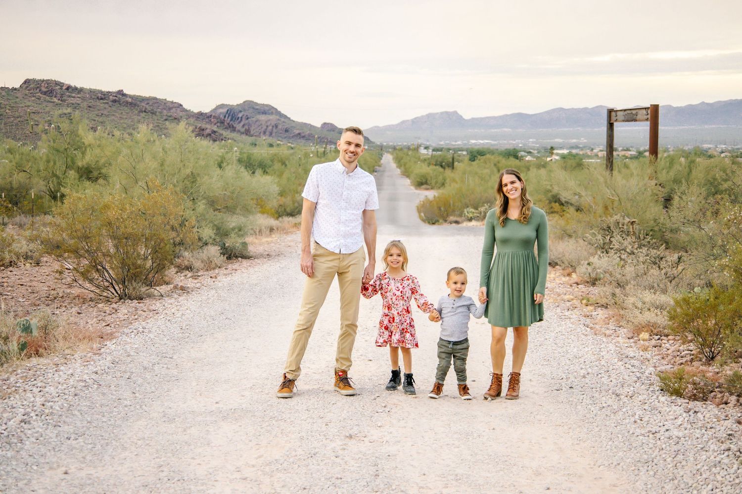 A family stands together on a desert path surrounded by mountains and desert vegetation in the background.