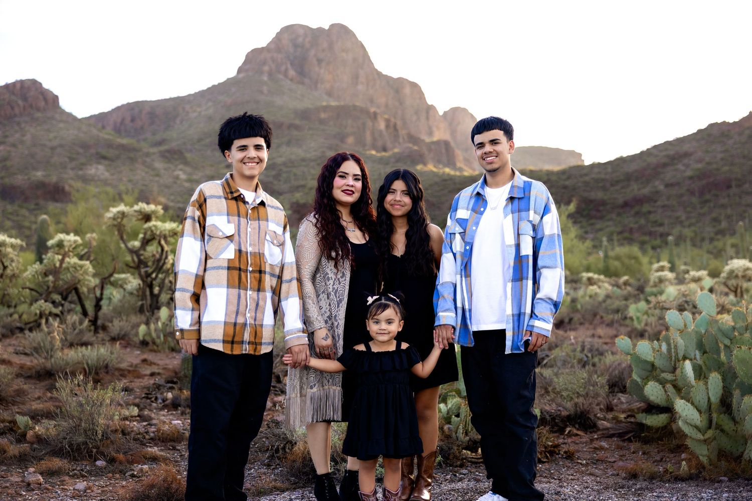 A family poses together in a desert landscape with mountains and cacti during golden hour.