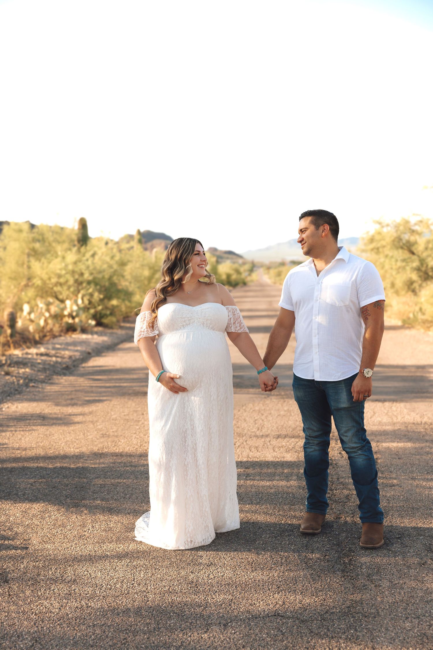 A couple in white and denim share an intimate moment in the desert during golden hour.