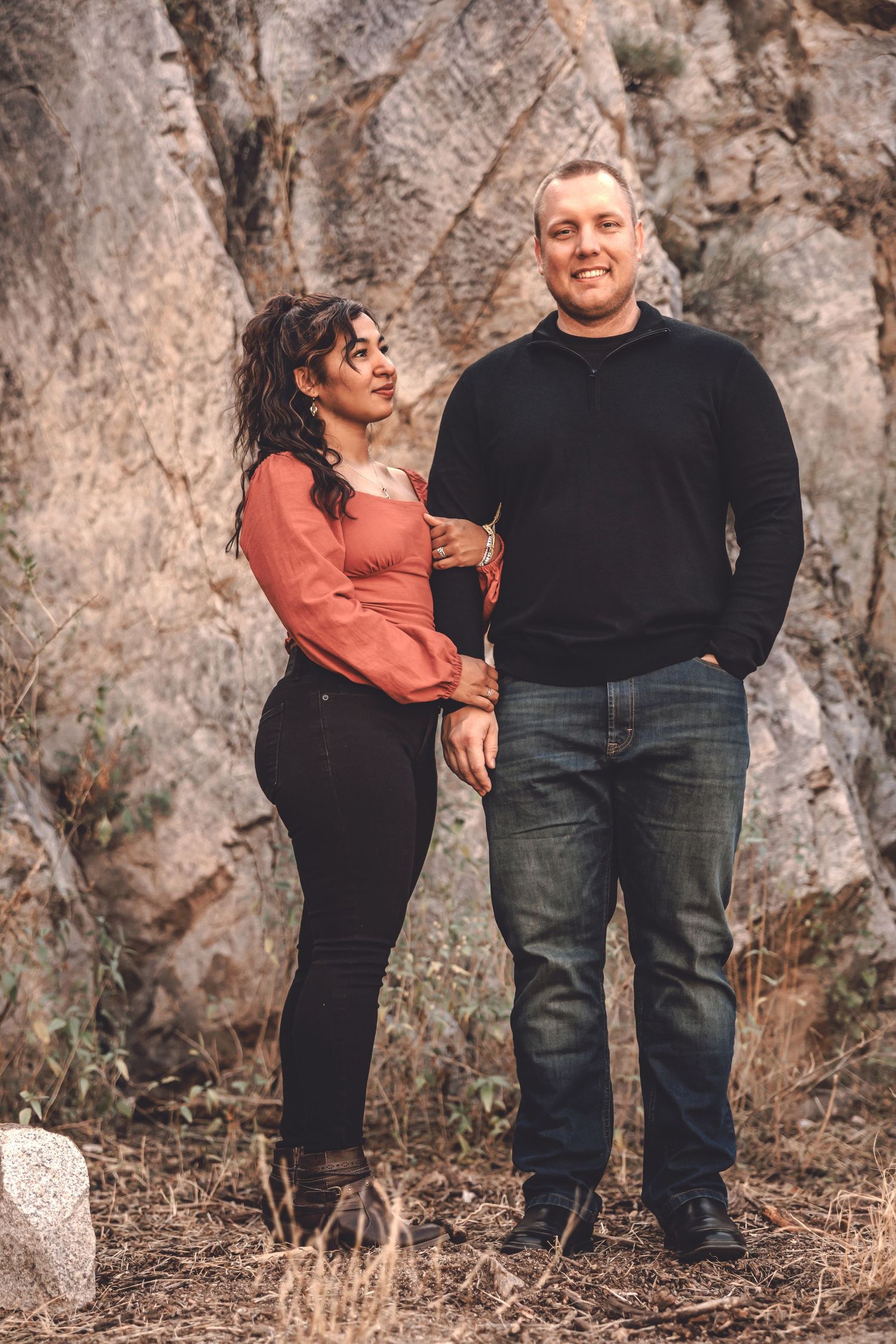 A couple shares a romantic moment against a rocky cliff backdrop in casual autumn attire.