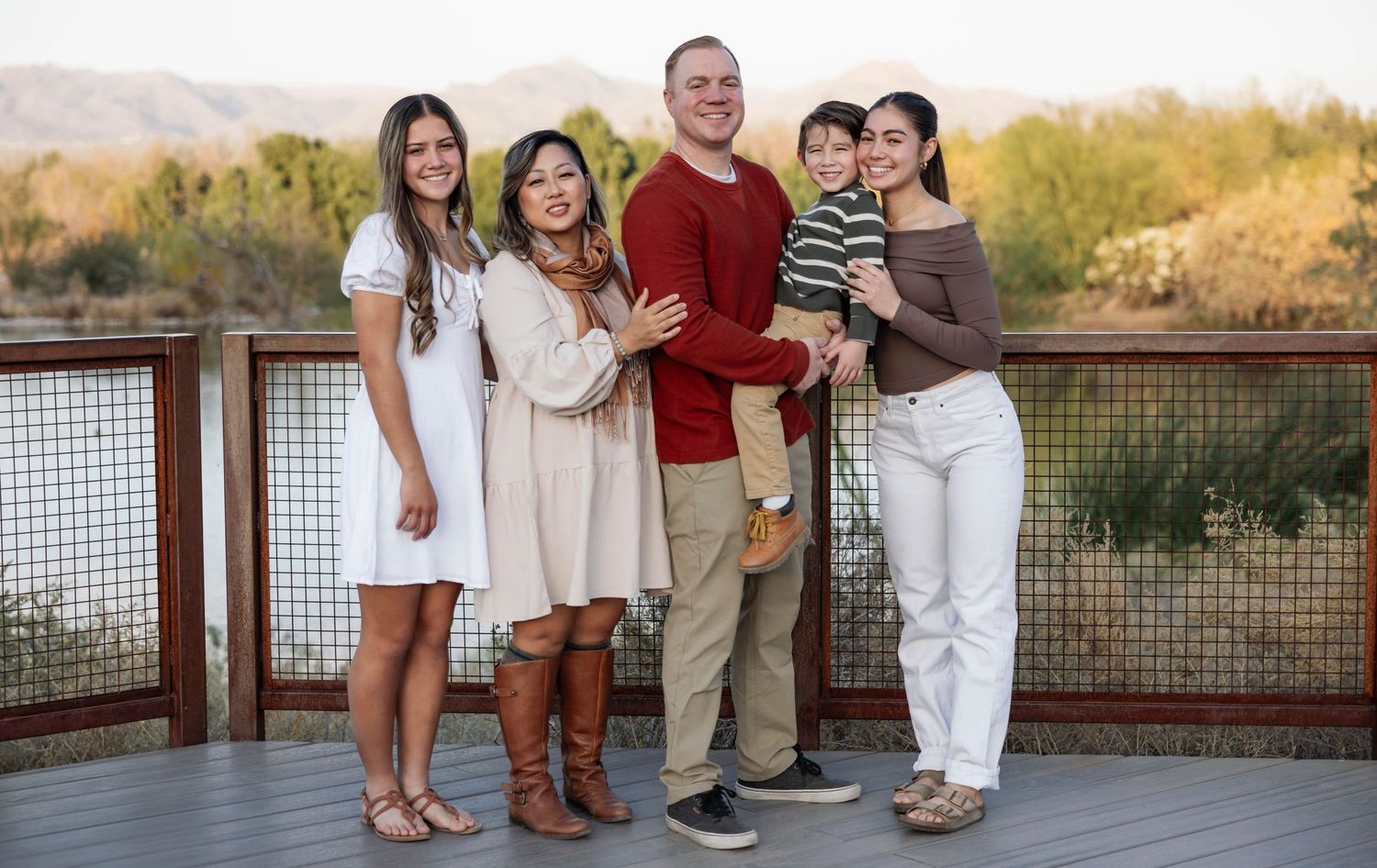 A group poses together in coordinating casual outfits on a wooden deck during golden hour.