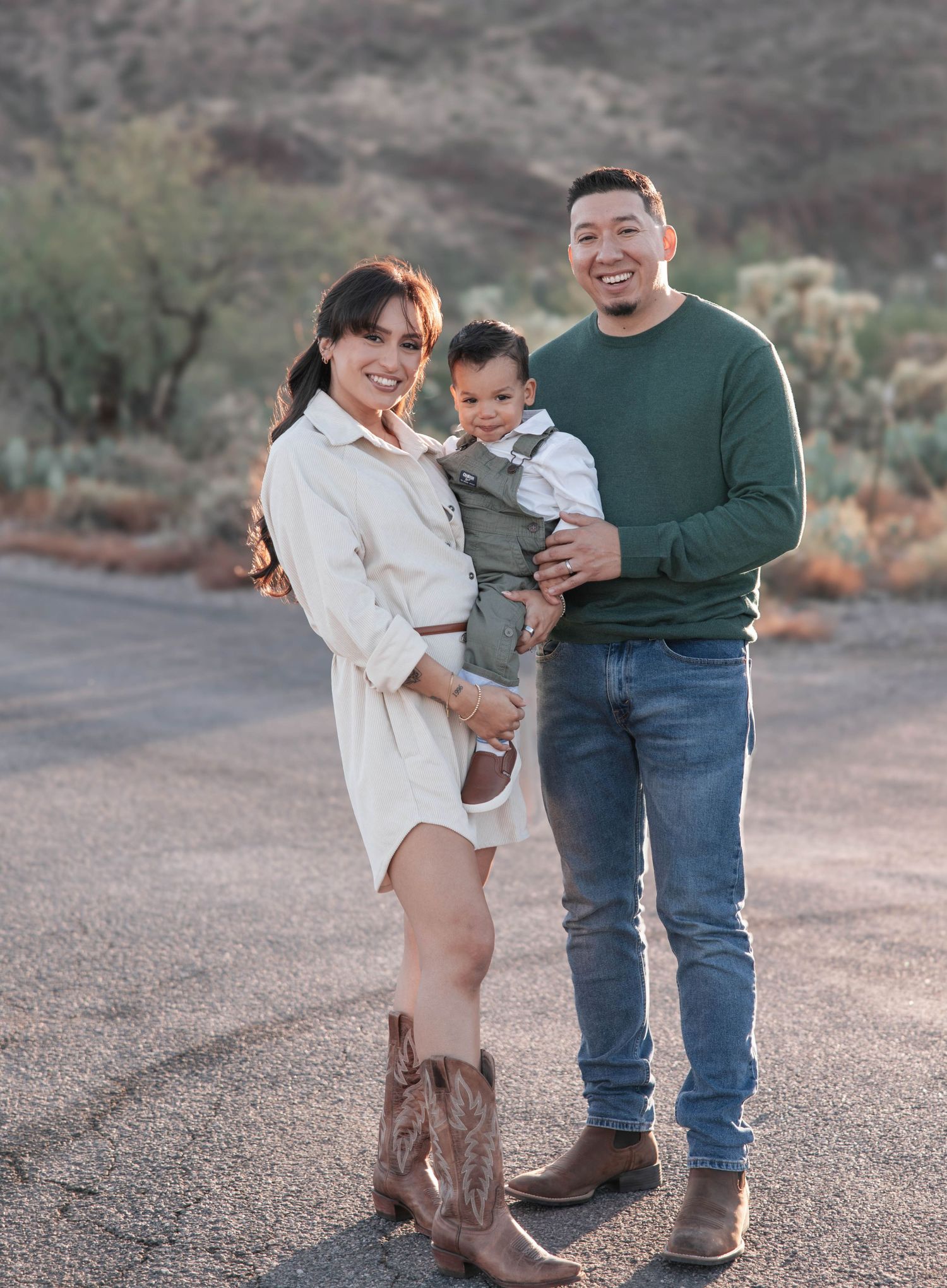 Casual family portrait in desert landscape with mountains and cacti in background.