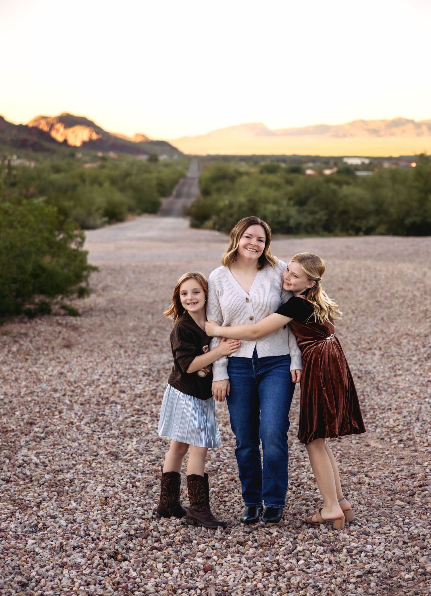 Three people pose together on a rocky desert landscape at sunset with mountains in the background.