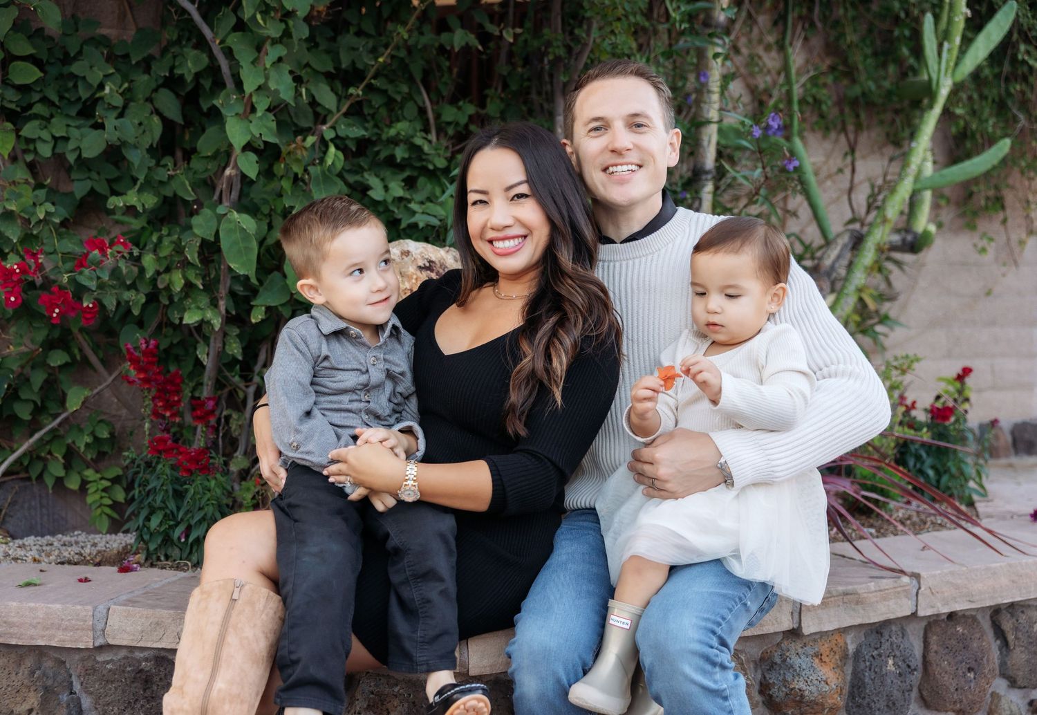 A series of casual outdoor family portraits taken against a rustic wall with greenery and red flowers.