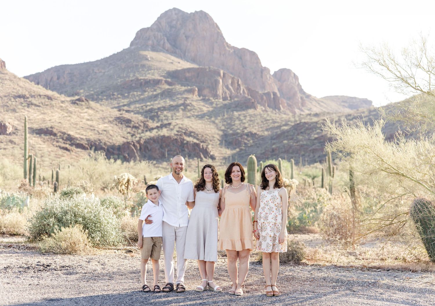 Family of five posing together in Arizona desert landscape with saguaro cacti and rocky mountain backdrop.