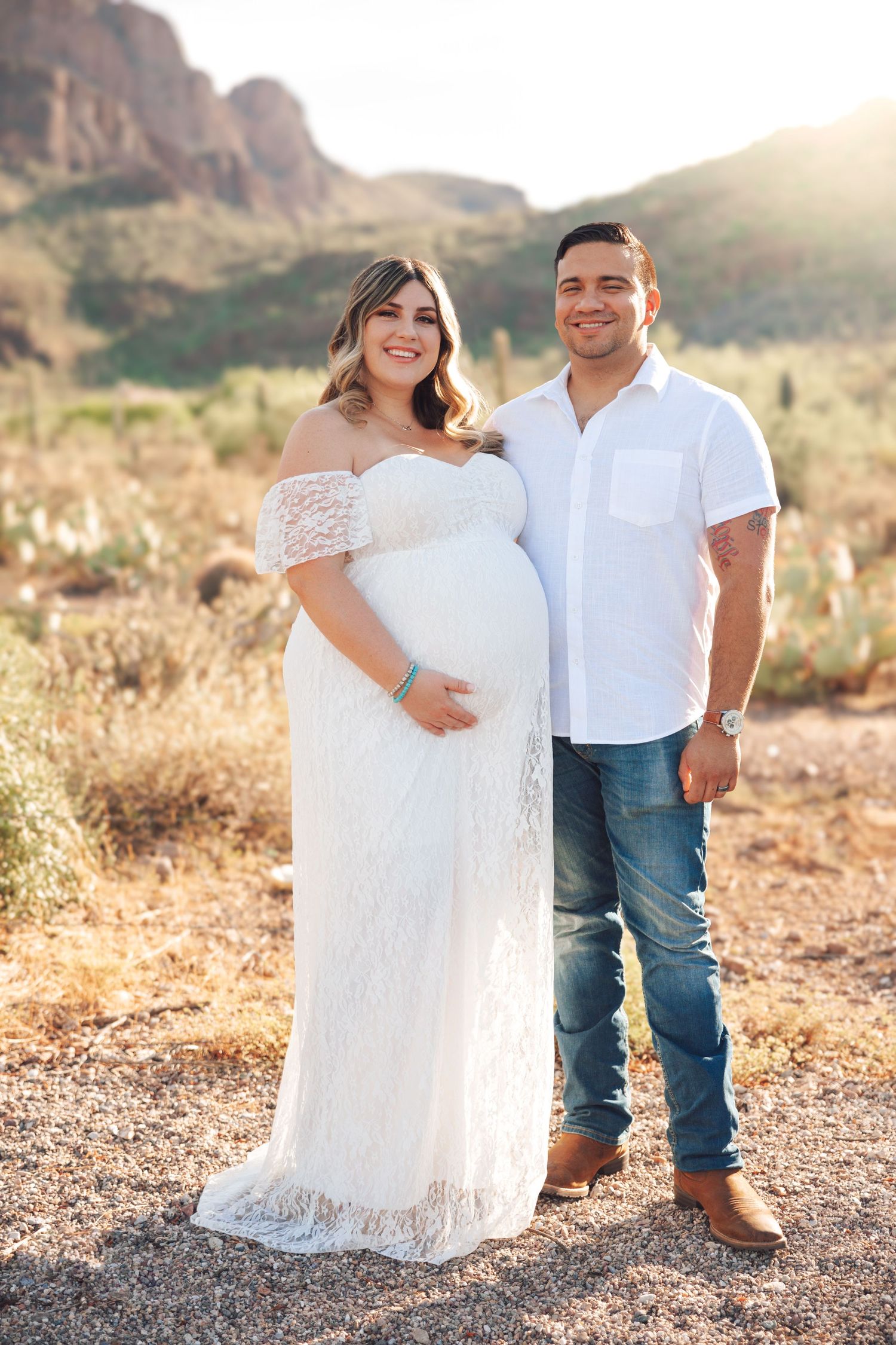 A couple in white and denim poses in the desert during golden hour with mountains in the background.