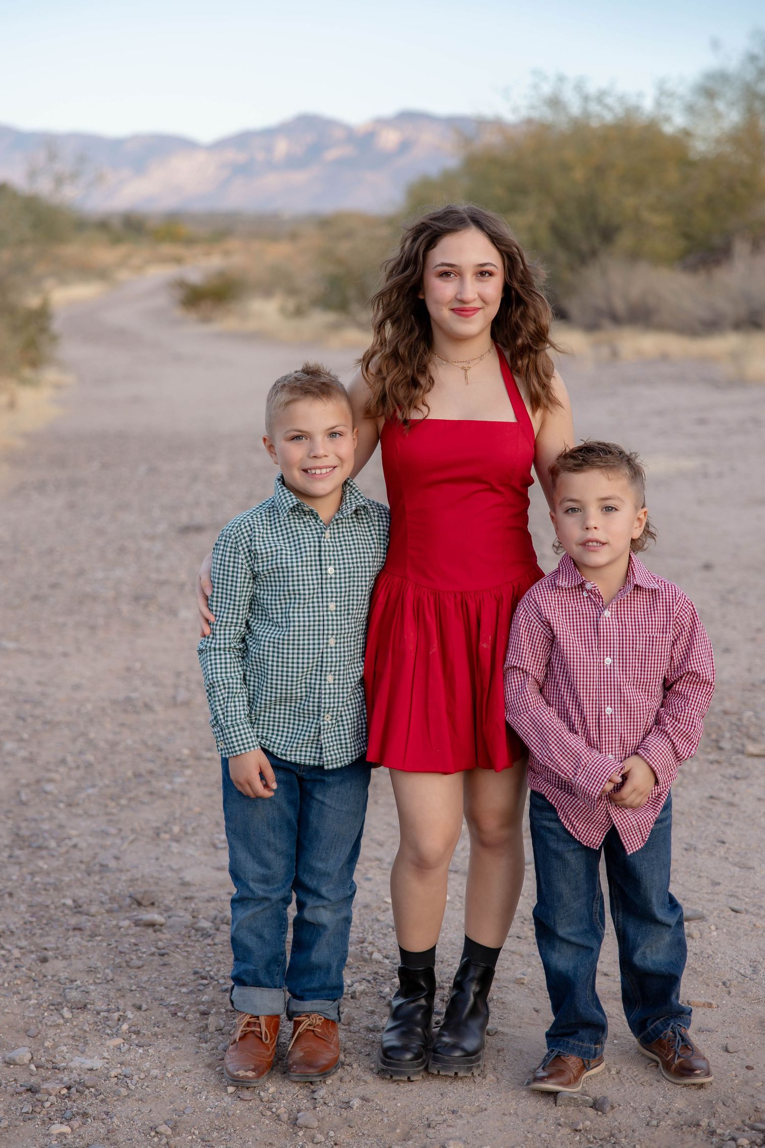 Three siblings pose together in a desert landscape with mountains in the background.