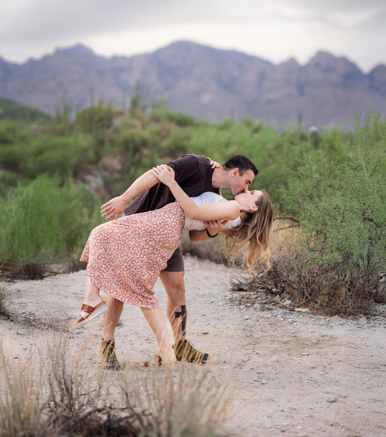 A couple dances and dips romantically in a desert landscape with mountains in the background.