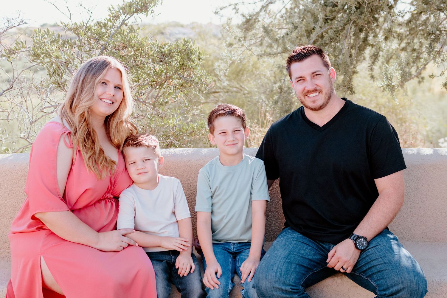 Family wearing coordinated coral and blue outfits sits together on outdoor steps for casual portrait session.