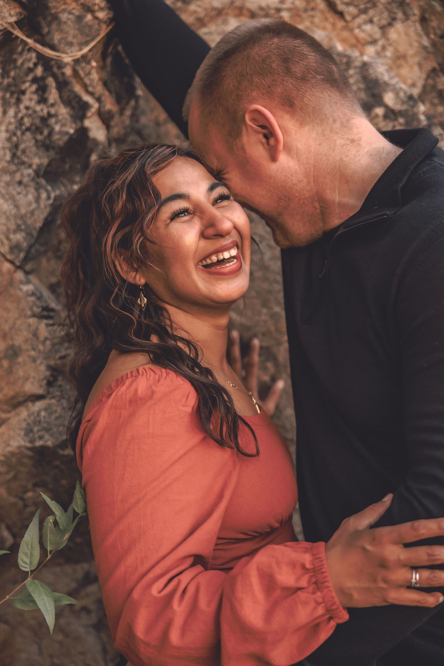 A romantic couple shares intimate moments against a textured rock wall background in warm lighting.