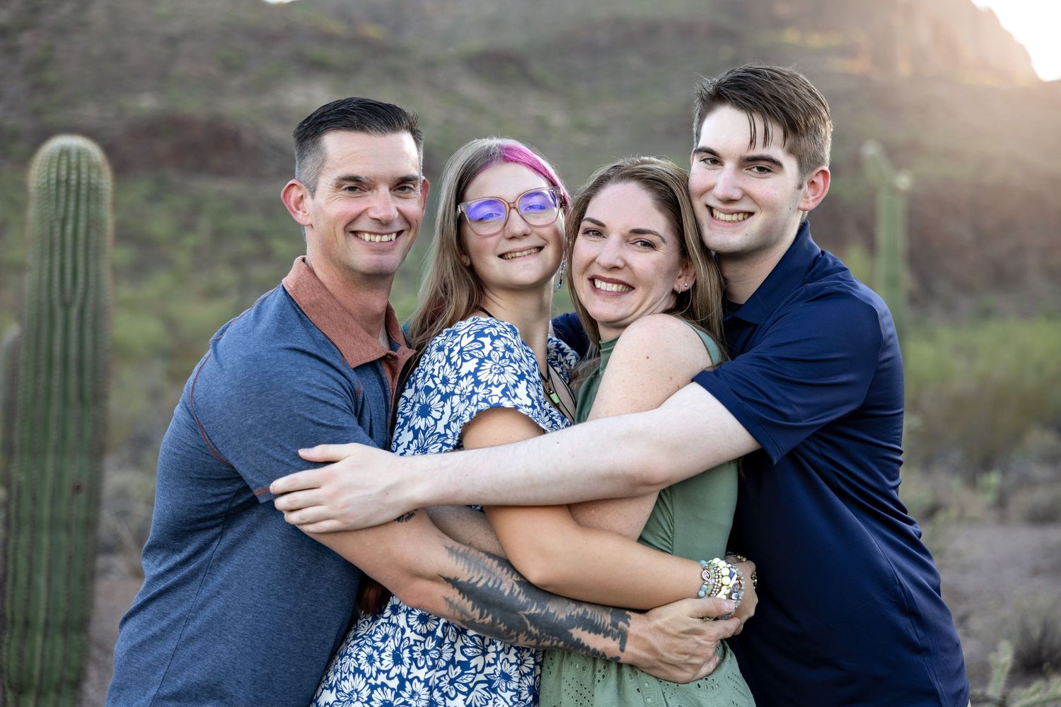 A group of people pose together outdoors in a desert landscape with saguaro cacti during golden hour.