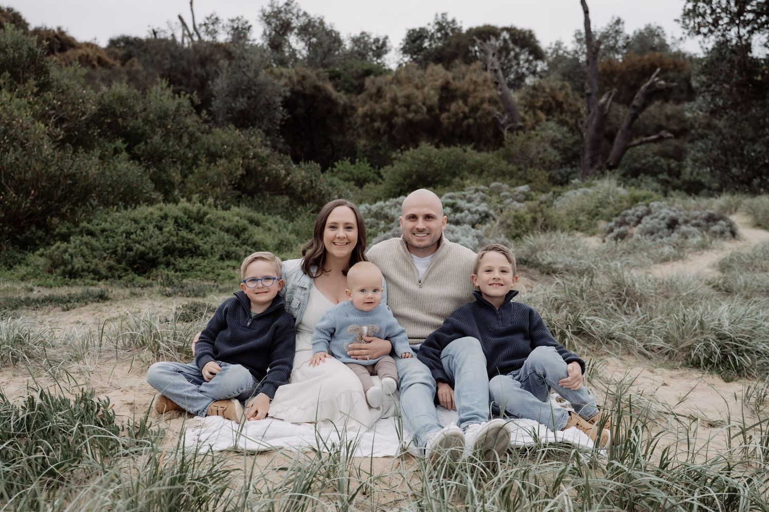 Family of five posing outdoors in a grassy field, parents with three young children smiling for a portrait photo.