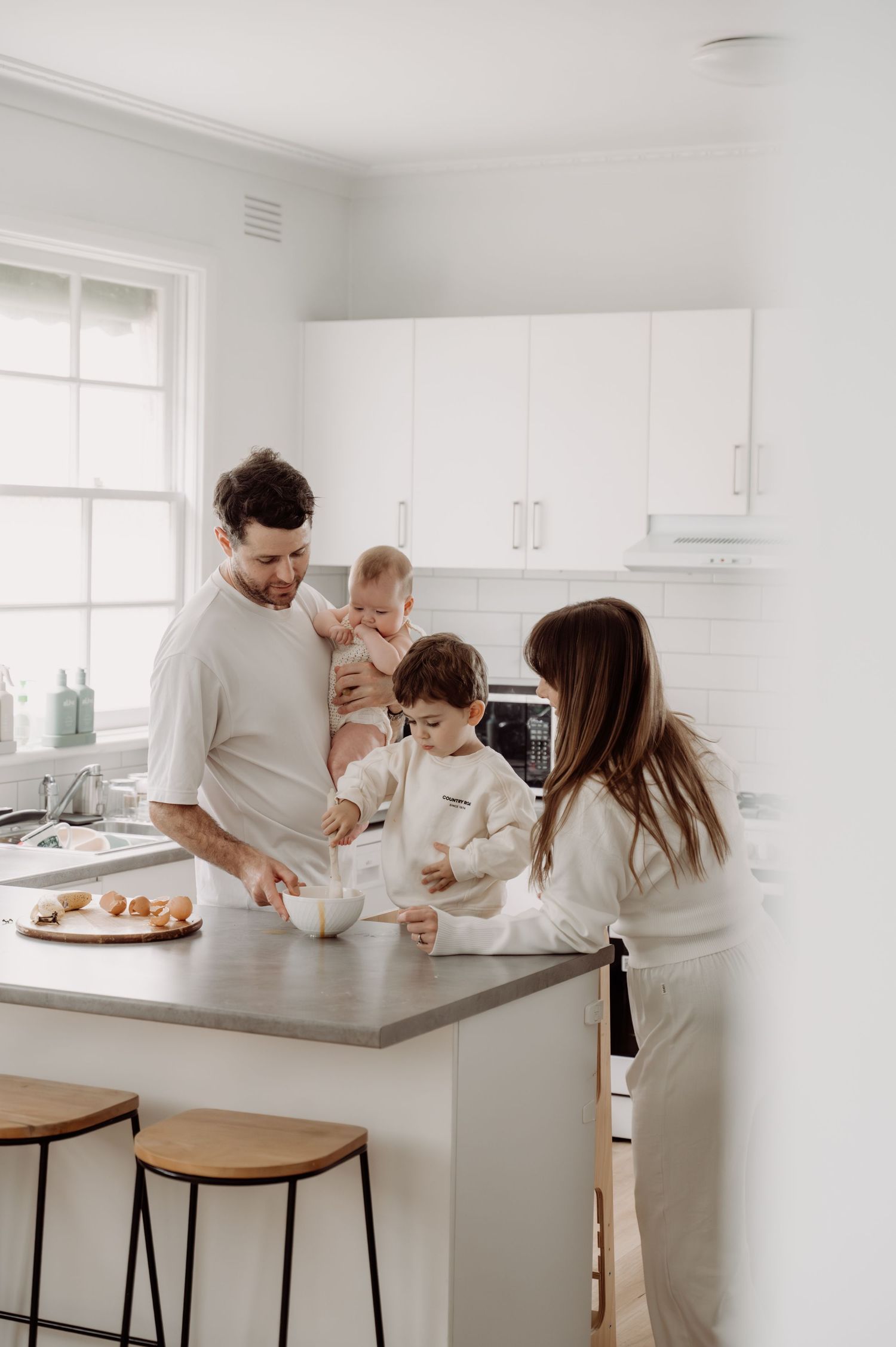 Family in matching white outfits cooking together in a bright modern kitchen.