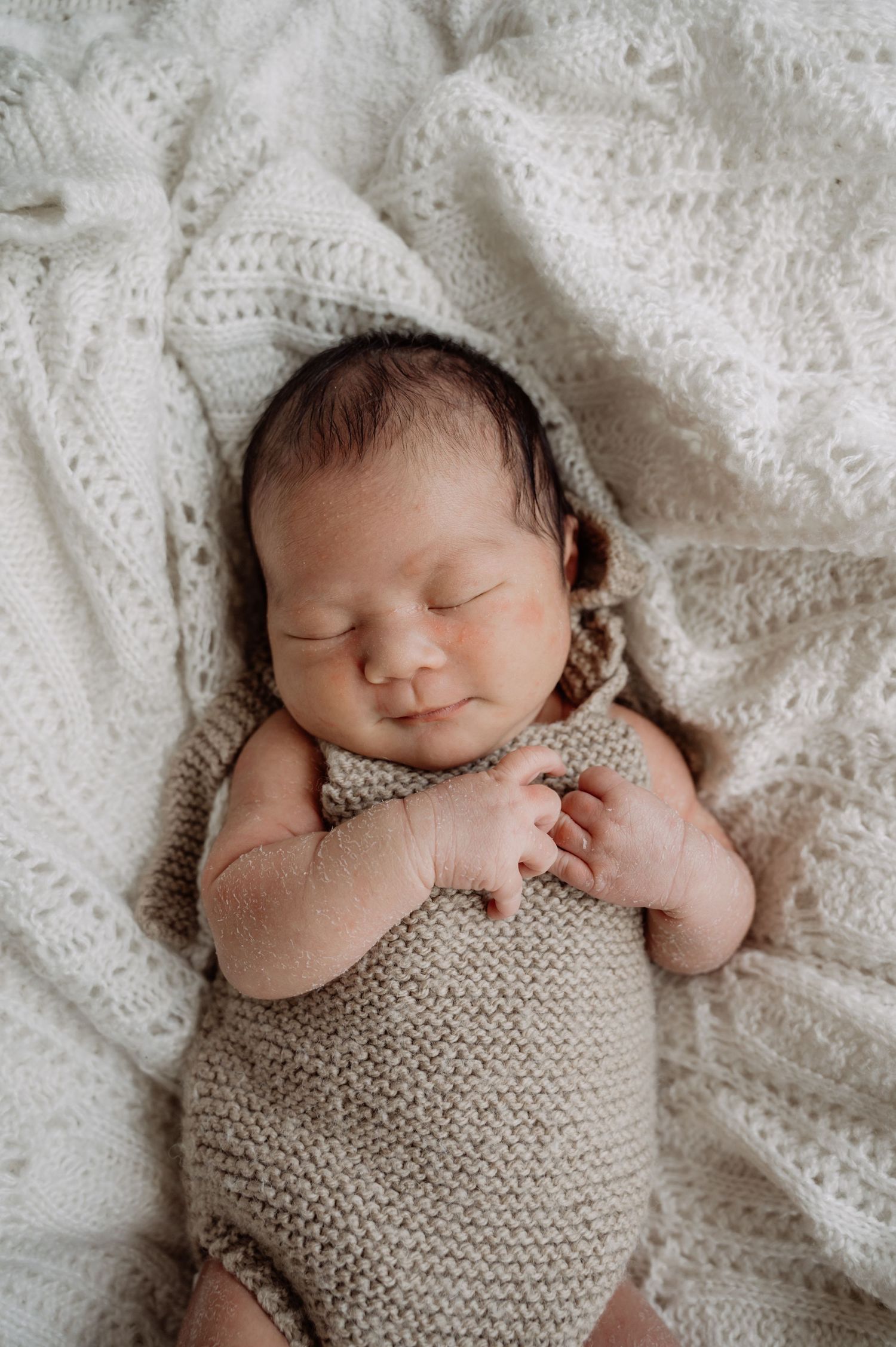 Peaceful sleeping newborn baby in a knit romper on a white crocheted blanket.
