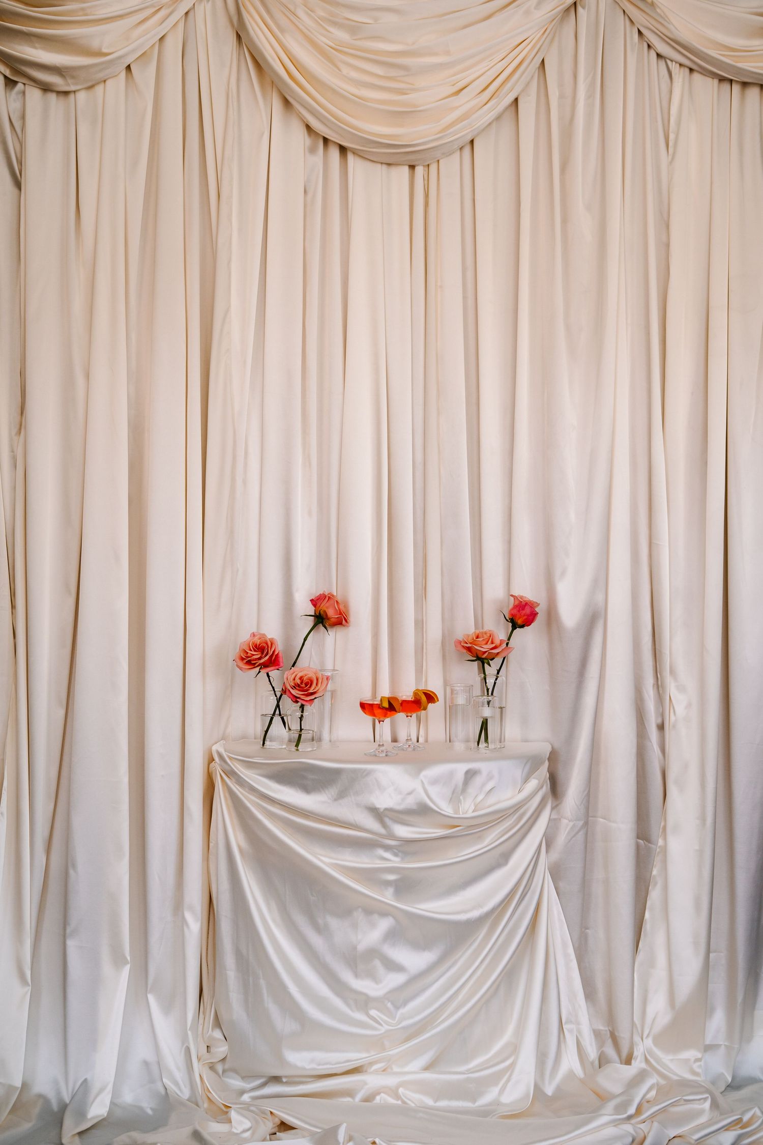 Elegant white draped fabric backdrop with coral flowers for wedding decoration.