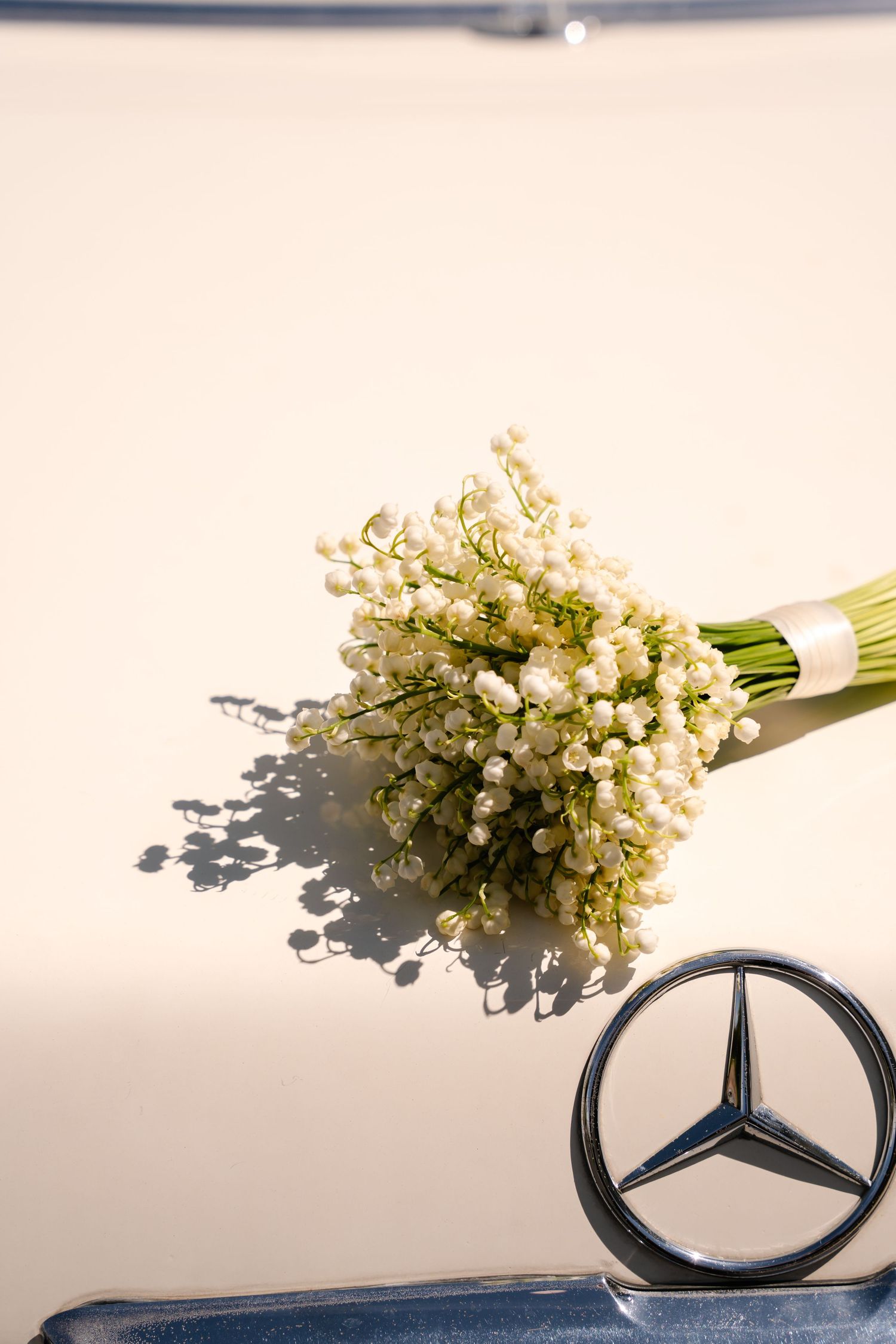 Lily of the valley bridal bouquet resting on a Mercedes-Benz hood ornament on a classic car.