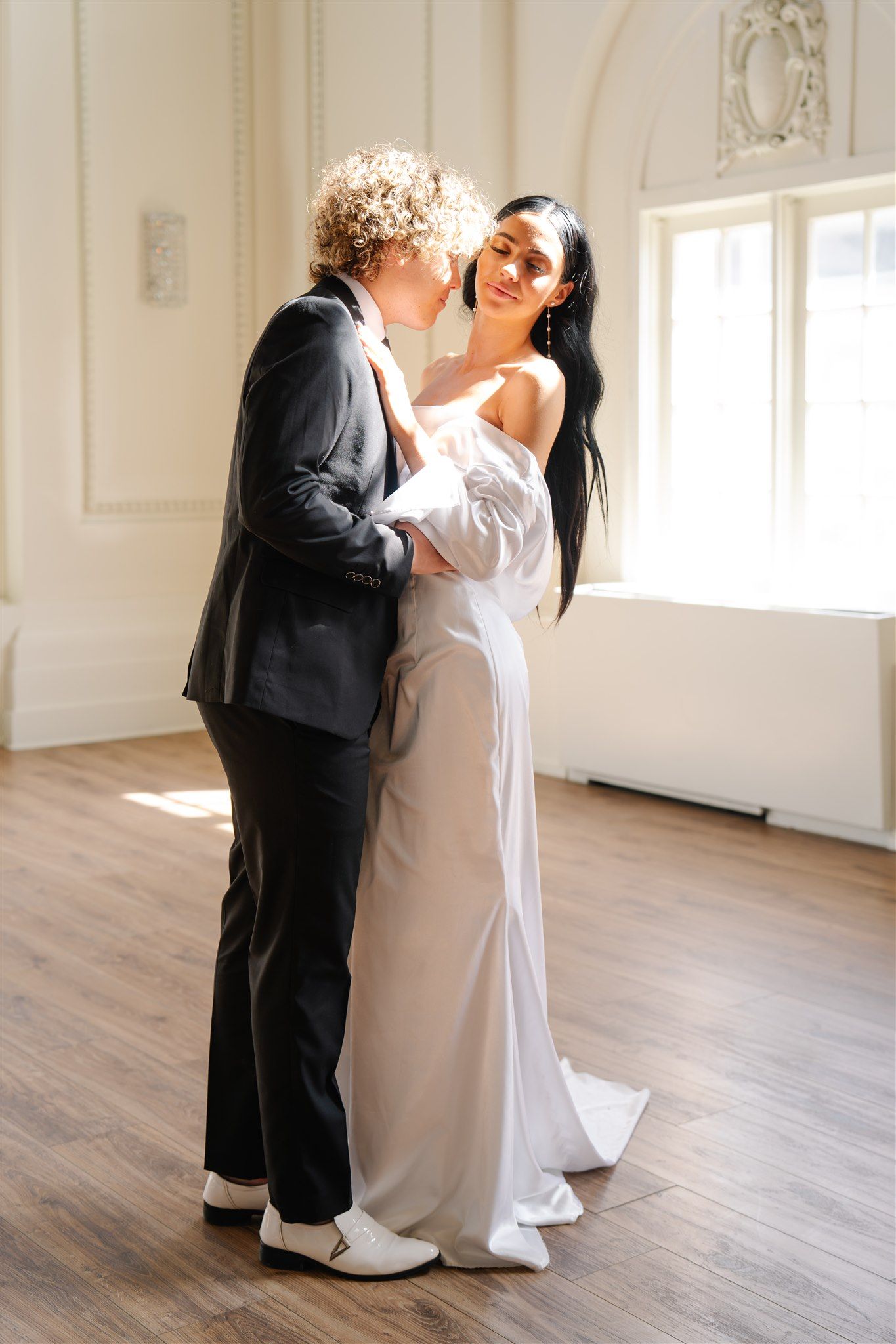 Couple shares an intimate dance moment in an elegant white room with hardwood floors.