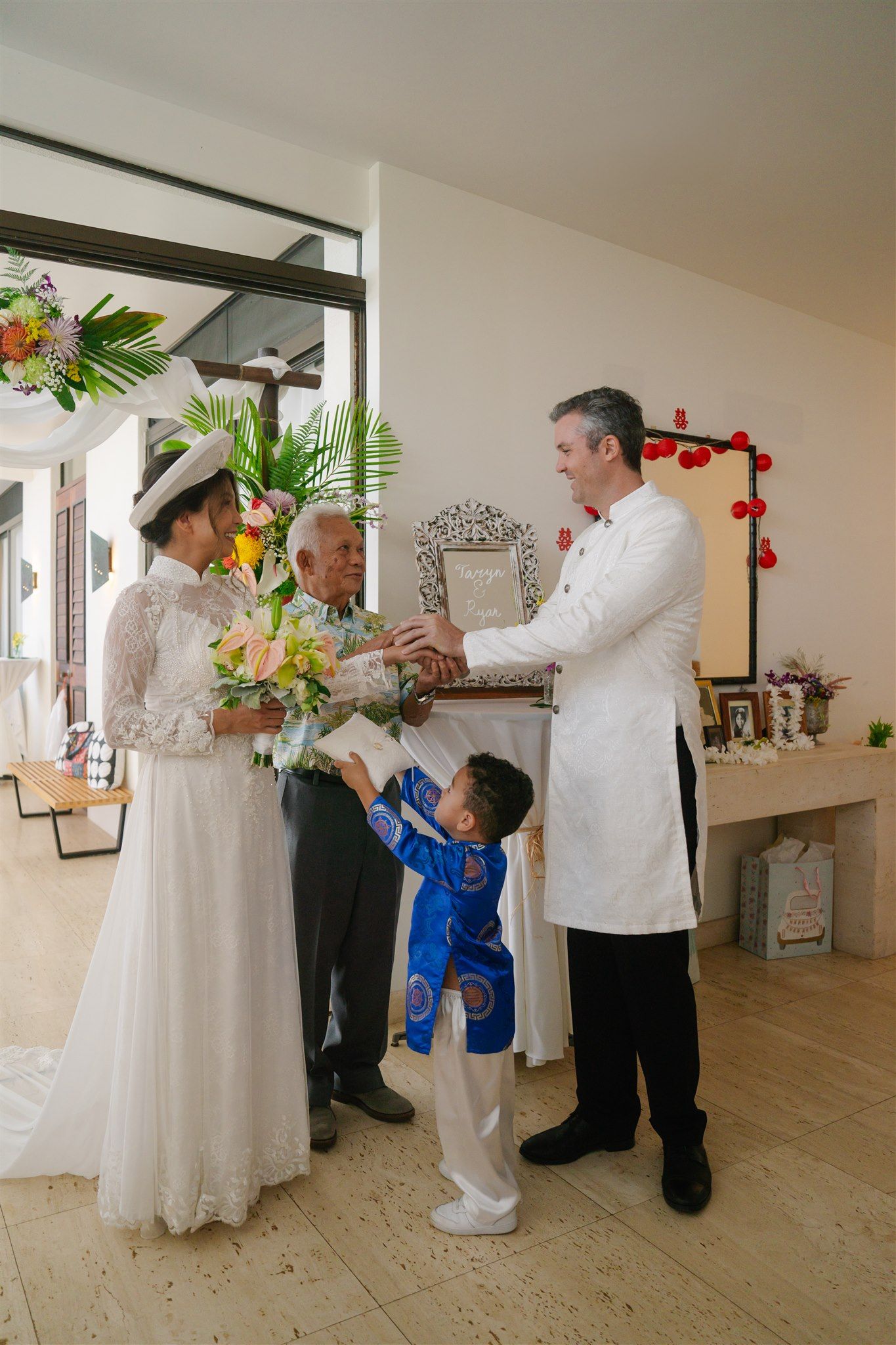 A wedding ceremony in a bright indoor space with white decor and tropical floral arrangements.