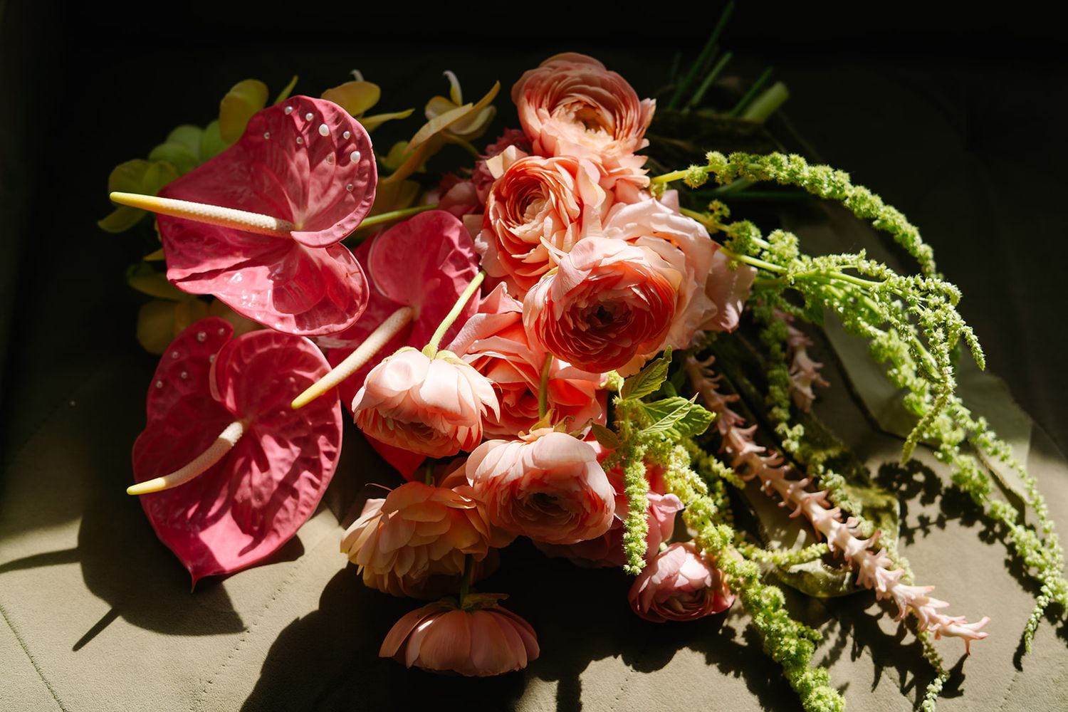 Pink and coral flowers with greenery arranged in dramatic lighting.
