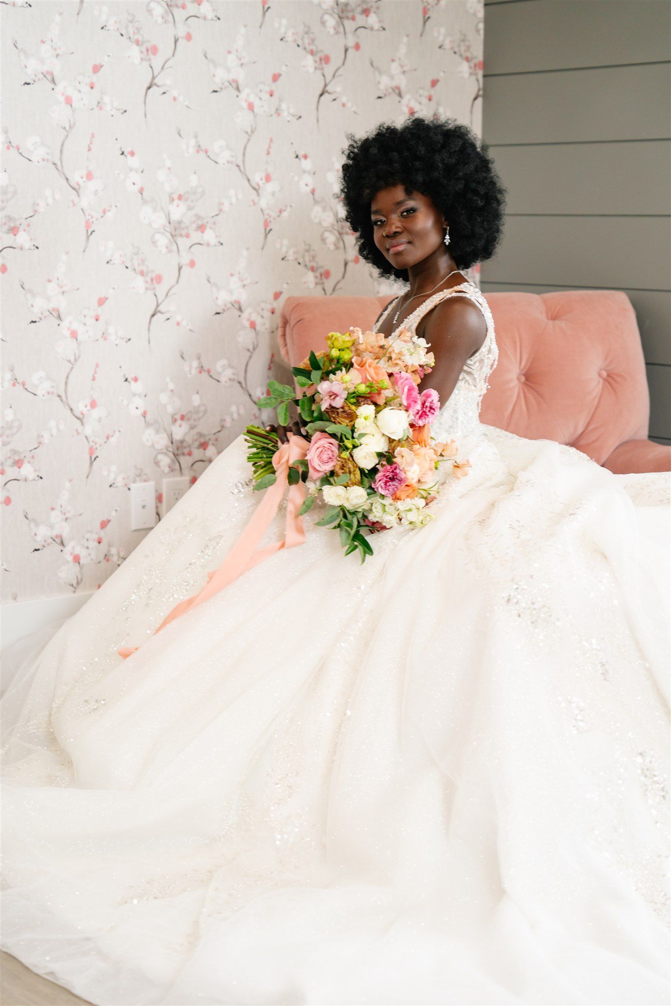 Elegant bridal portrait on pink sofa with peach and coral floral bouquet.