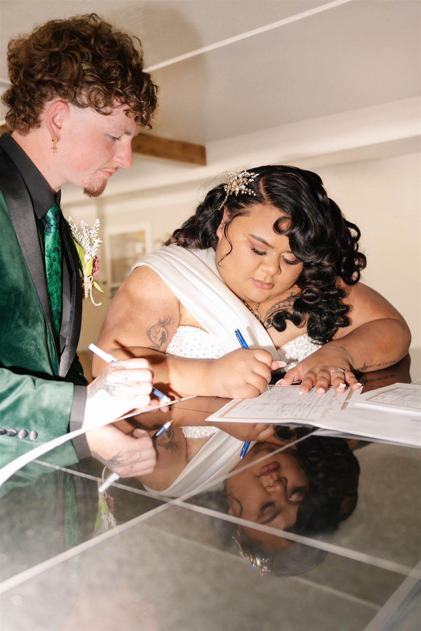 Wedding couple signs documents together at a reflective table surface.