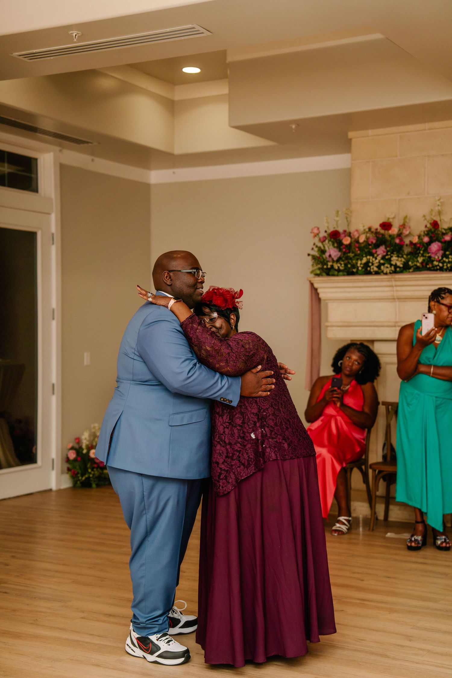 Emotional embrace during wedding reception with guests in formal attire watching.