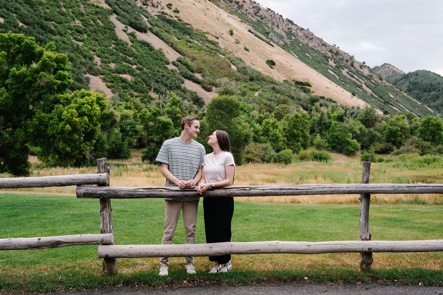 A couple sits together on a wooden bench with mountain views in the background.