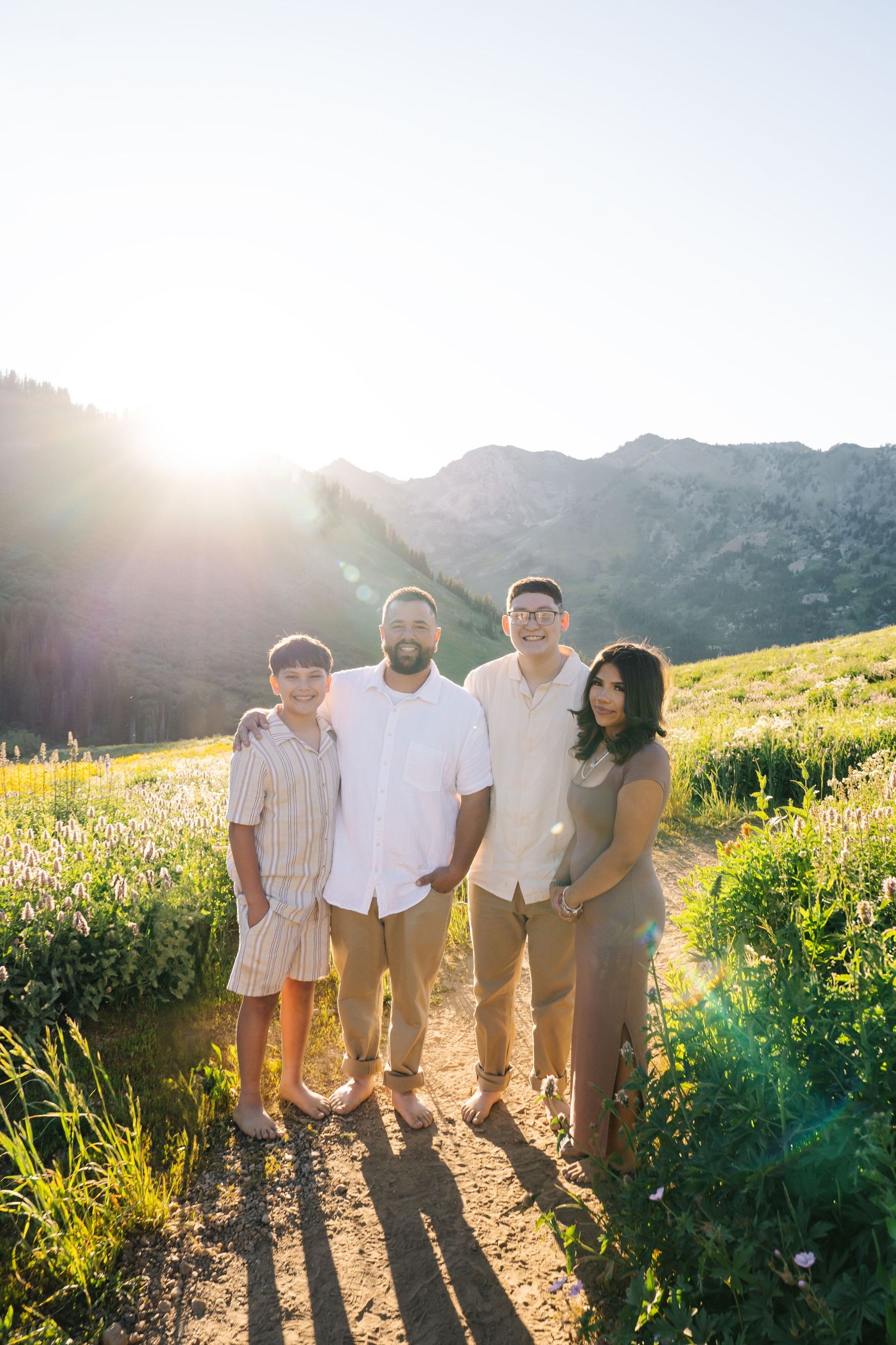 Family of four posing on a mountain trail surrounded by wildflowers during golden hour sunset.