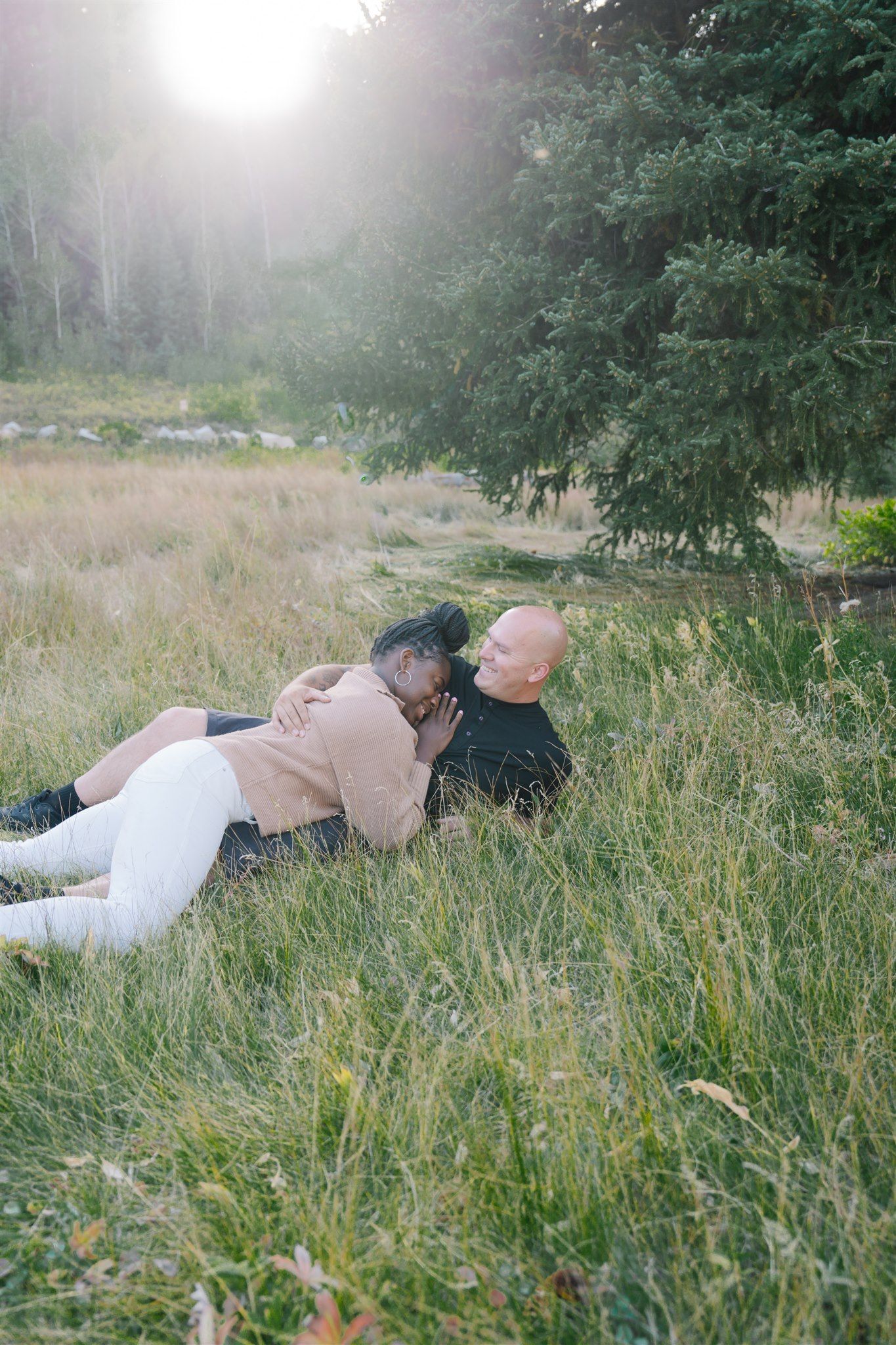 Couple lying in tall grass during a misty outdoor photoshoot.