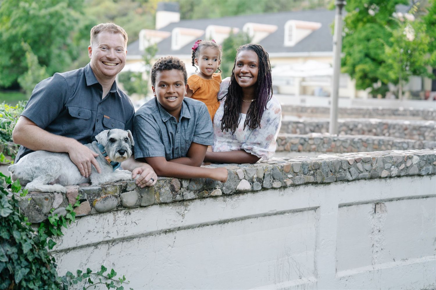 Family sitting together on a stone wall with their dog during an outdoor photoshoot.