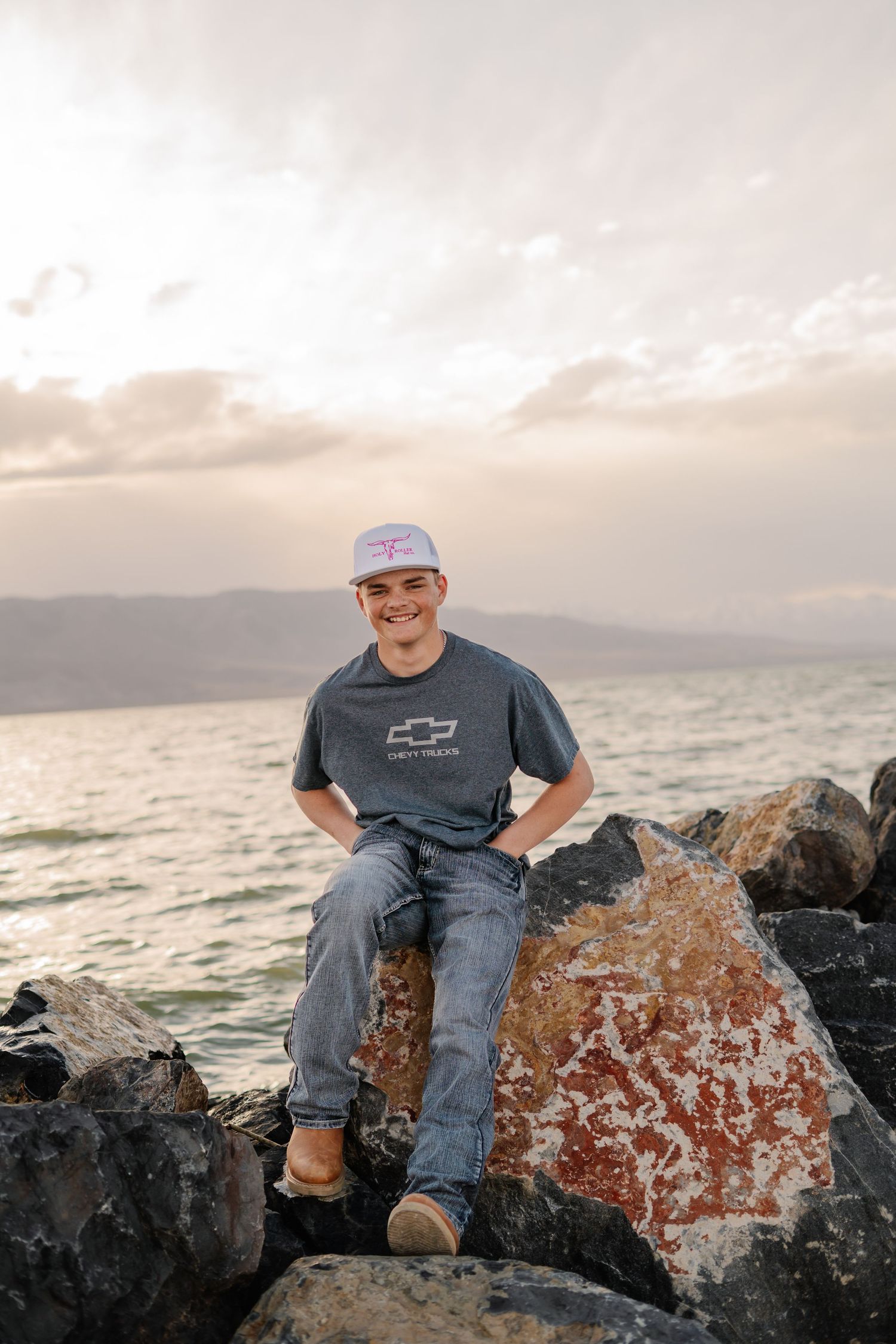 Person sitting on coastal rocks at sunset with ocean view in background.