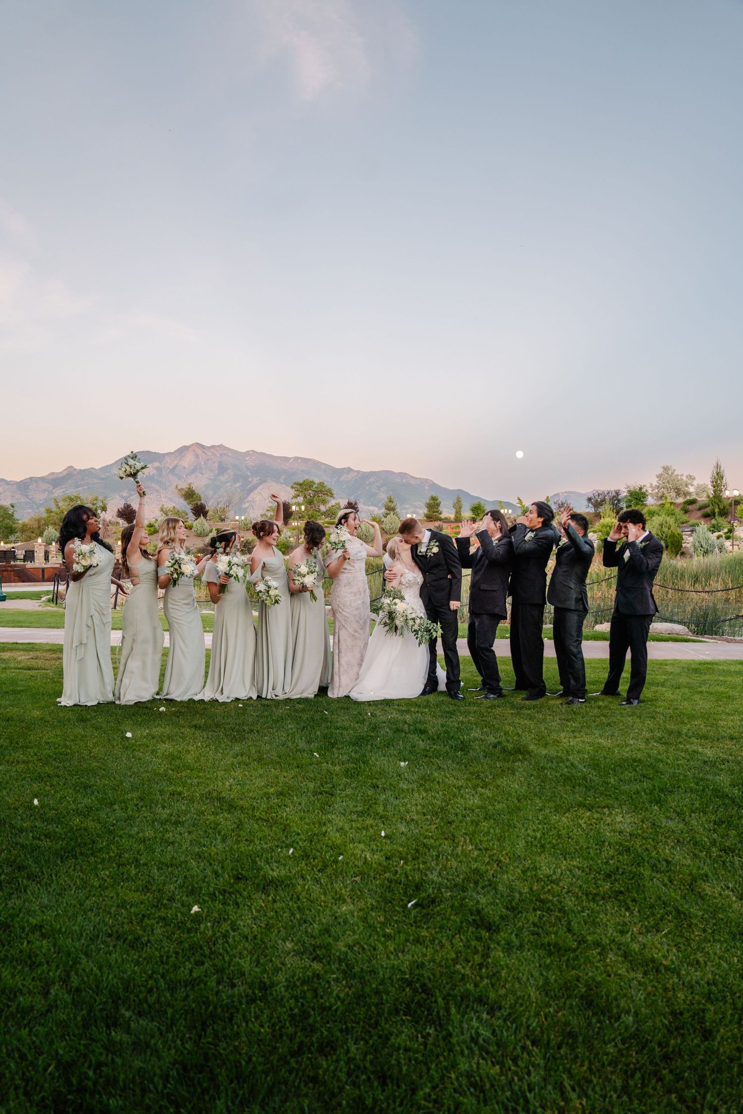 Wedding party poses on a grassy lawn at sunset with mountains in the background.
