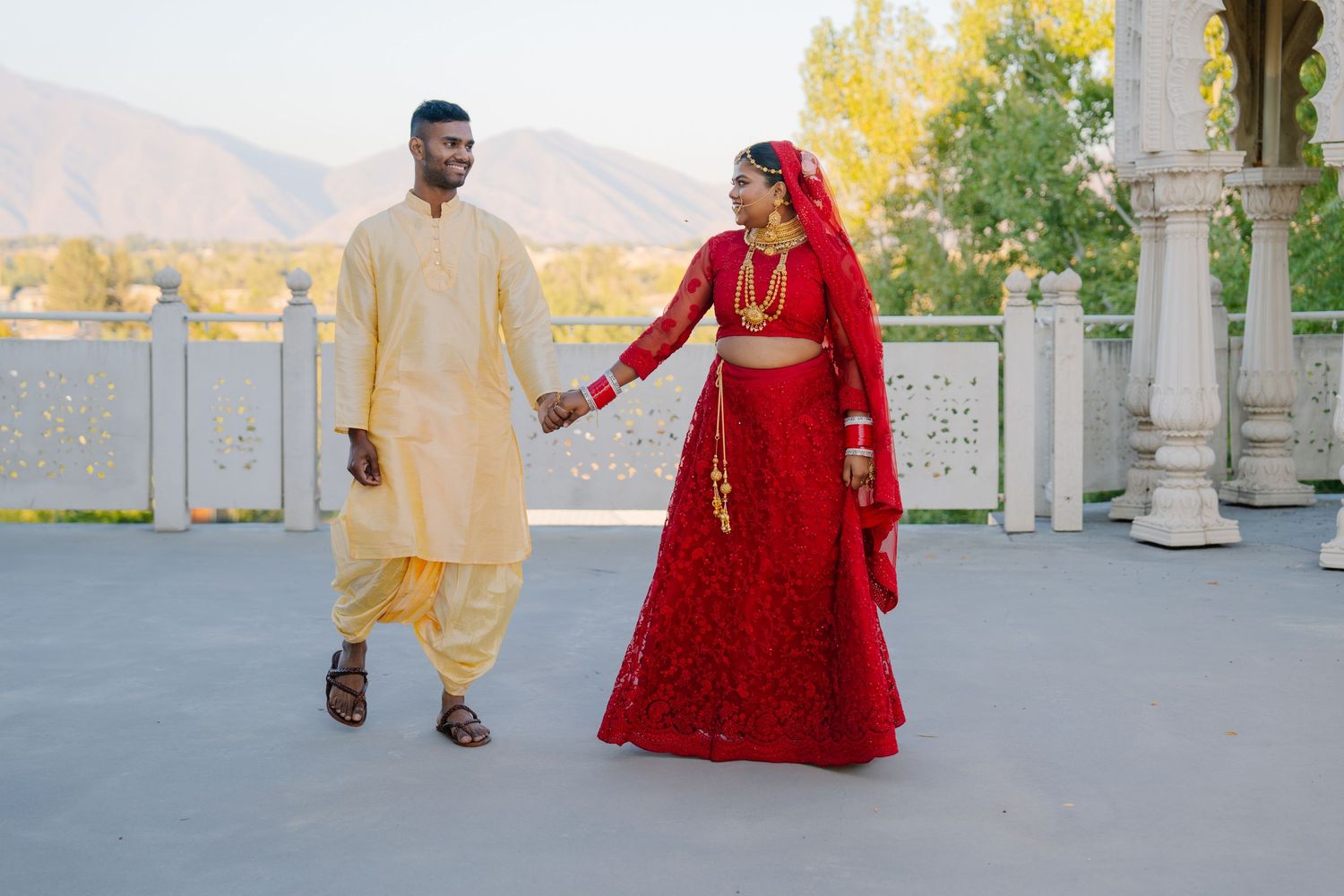A wedding couple in yellow and red attire poses in an outdoor pavilion setting.