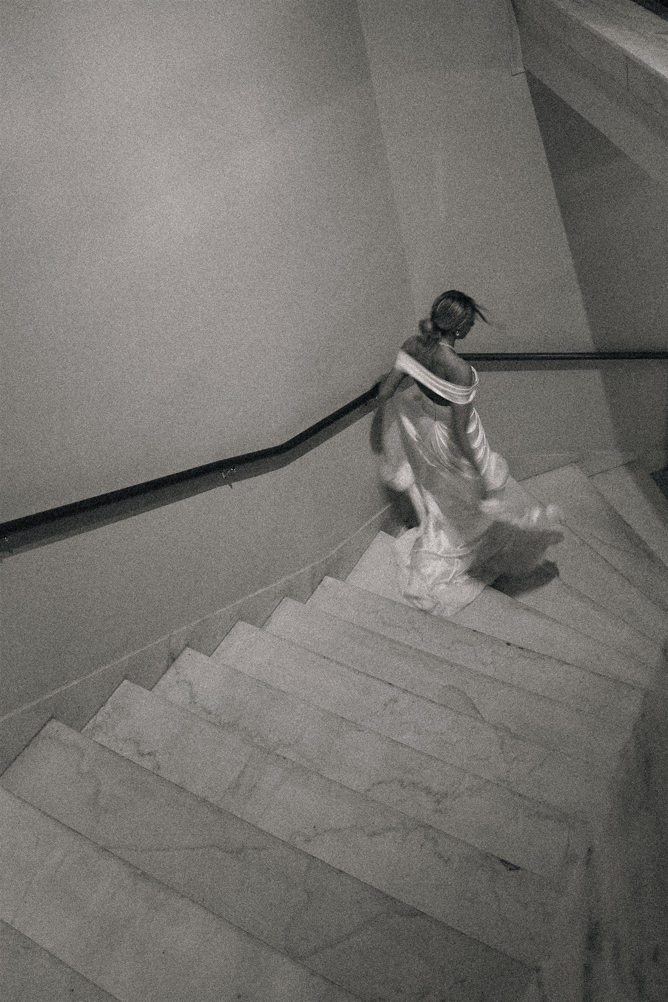 Wedding dress flowing down concrete stairs in dramatic black and white photography.