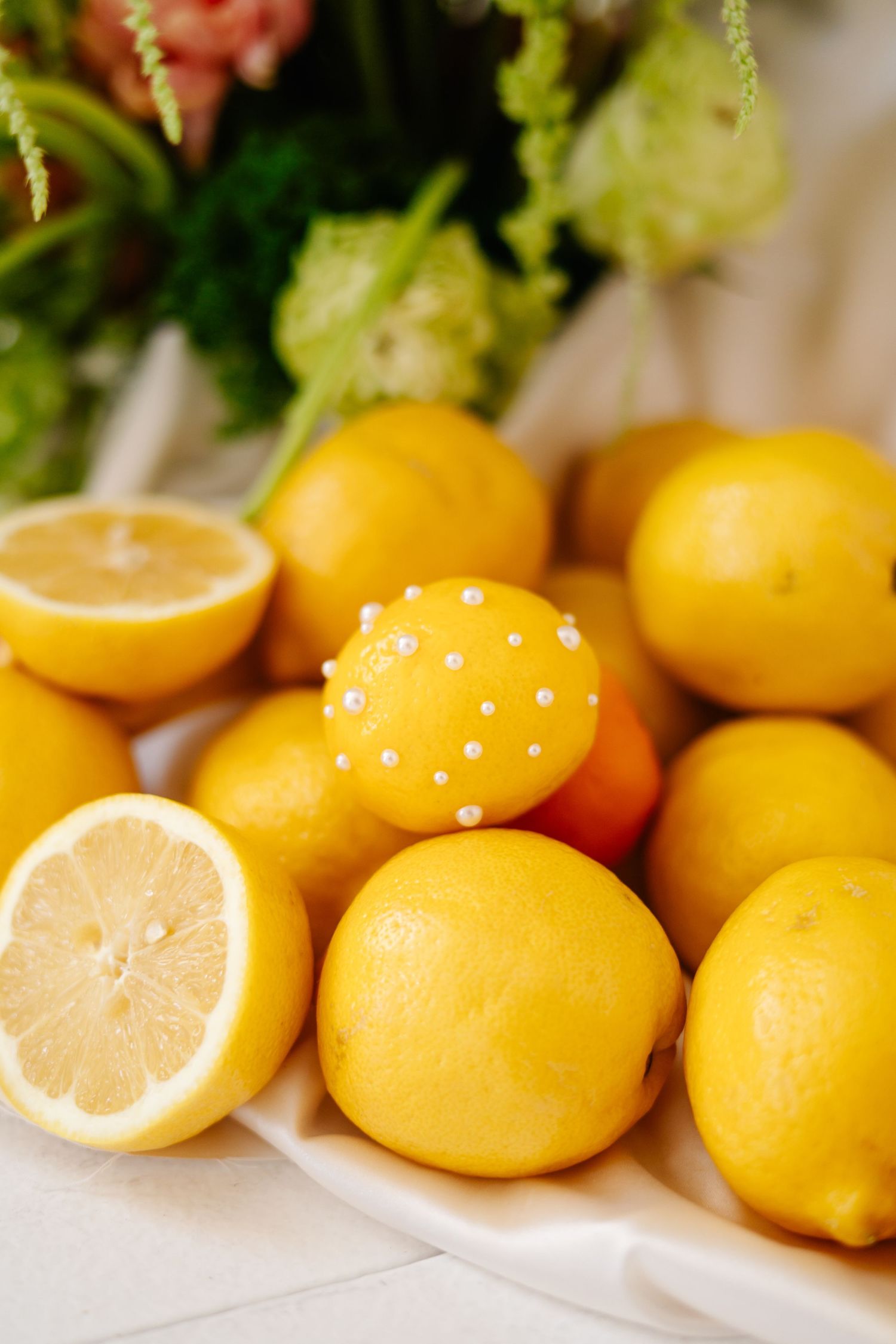 Fresh yellow lemons decorated with pearl pins arranged on white surface.